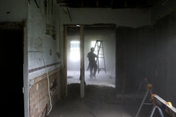 Dust from insulation in a ceiling being torn down obscures Josh Stewart, crew-chief-in-training for Better Homes Minnesota, a non-profits that assists