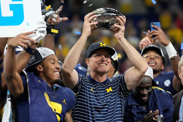 FILE - Michigan head coach Jim Harbaugh holds the trophy as he celebrates with his team after defeating Purdue in the Big Ten championship NCAA colleg