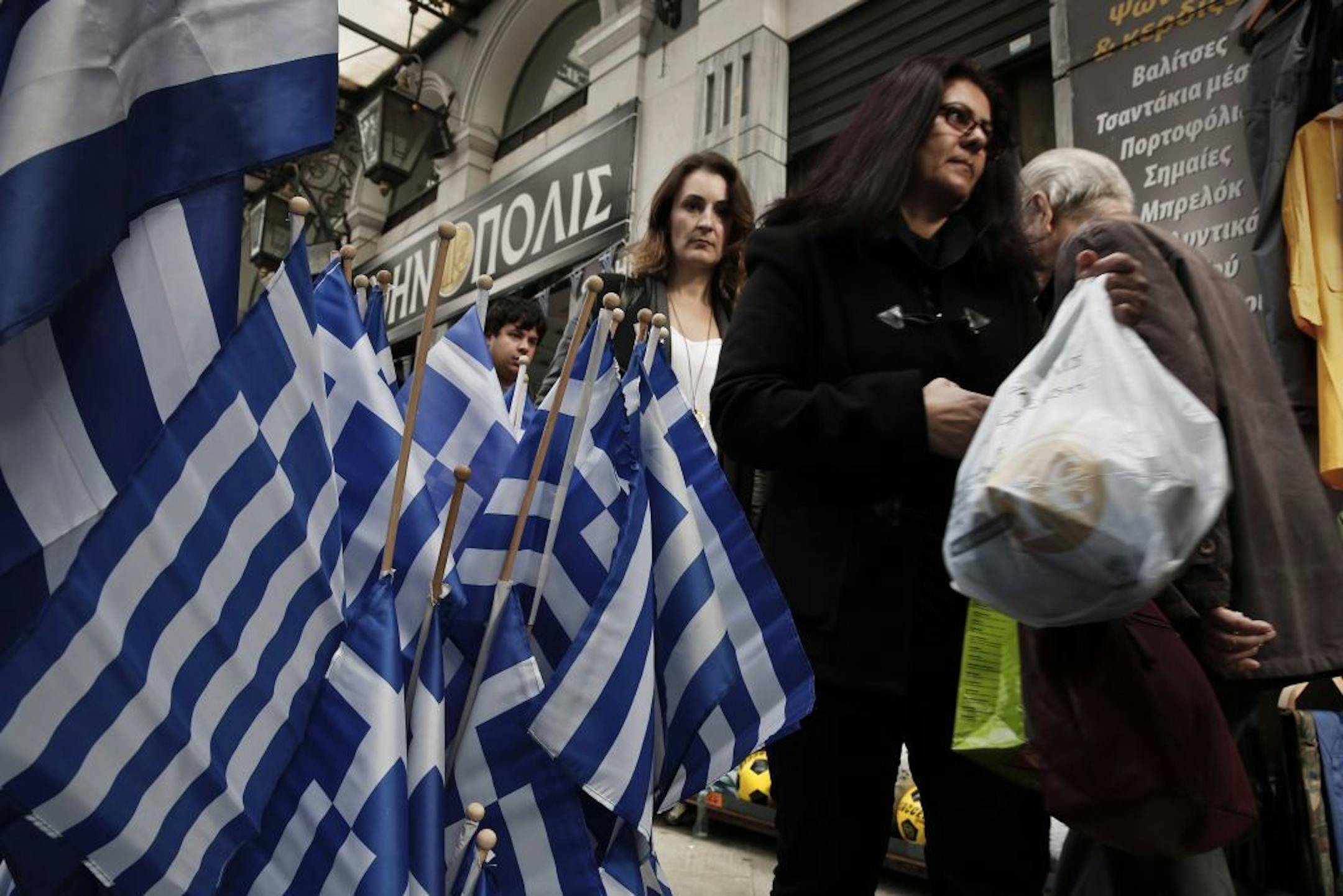 Pedestrians walk past Greek flags for sale in central Athens, Tuesday, Dec. 9, 2014. The Athens benchmark index tumbled 10.5 percent in midday trading Tuesday, the biggest one-day drop since 1987, after the conservative-led government brought forward the date of a presidential vote. If the vote proves inconclusive, it could lead to general elections.