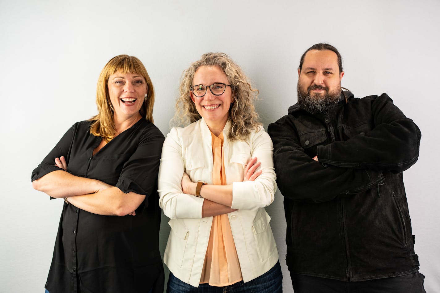 Two women and a man pose for a portrait while smiling and crossing their arms.