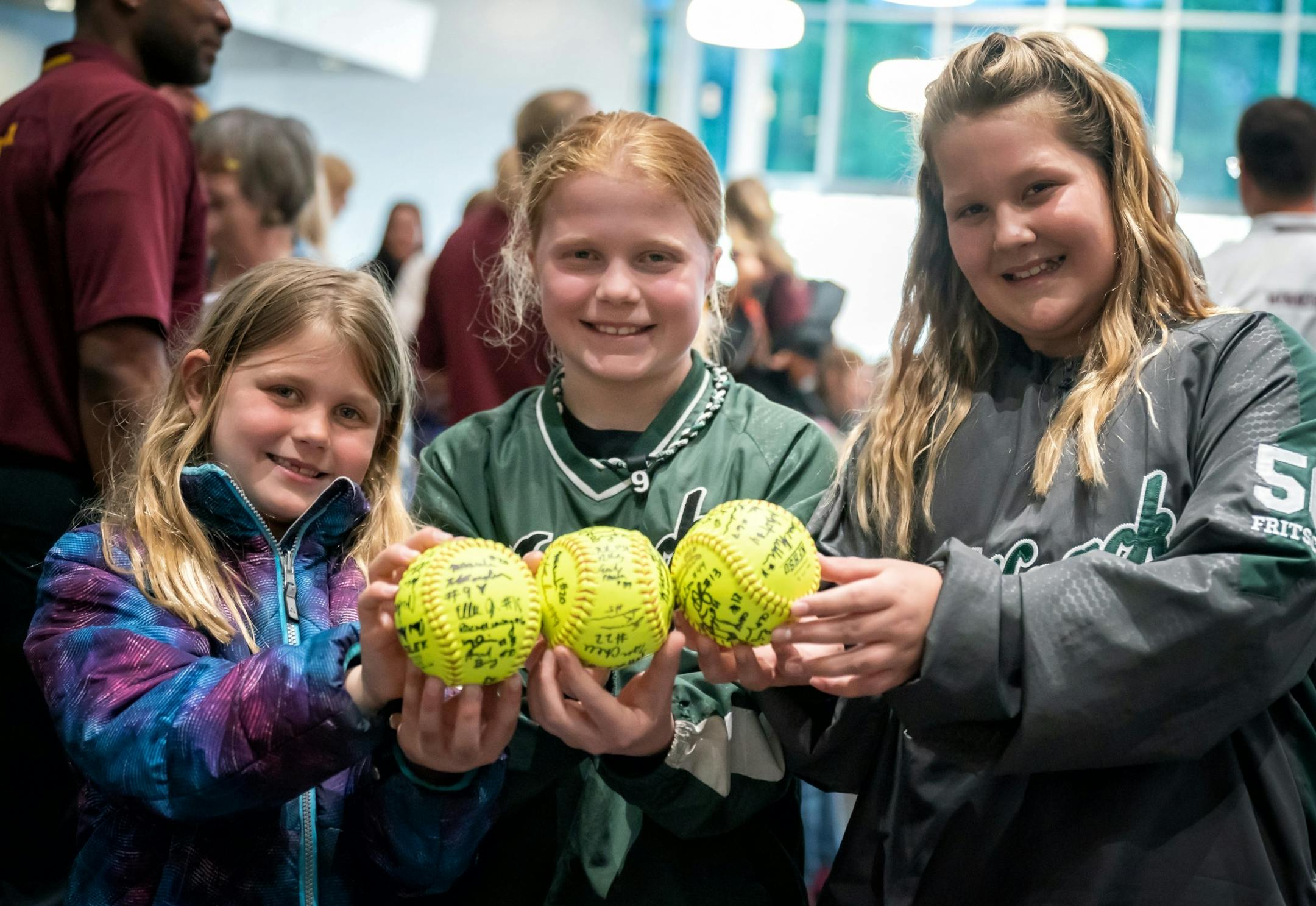 Madelyn Youngquist, 7, Ava Youngquist, 11, and their friend Stella Fritsche, 10 held up their autographed softballs. Their mom said she brought the girls to inspire them, so they can see what happens with hard work. The Gophers softball team has a rally/autograph session before heading to Oklahoma City for the Women's College World Series. This was in the lobby of the Athletes Village.