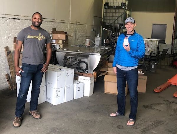 Du Nord Craft Spirits owner Chris Montana (left) donates hand sanitizer to Lonny Evans (right) of Loaves & Fishes, the state’s largest free meal pro