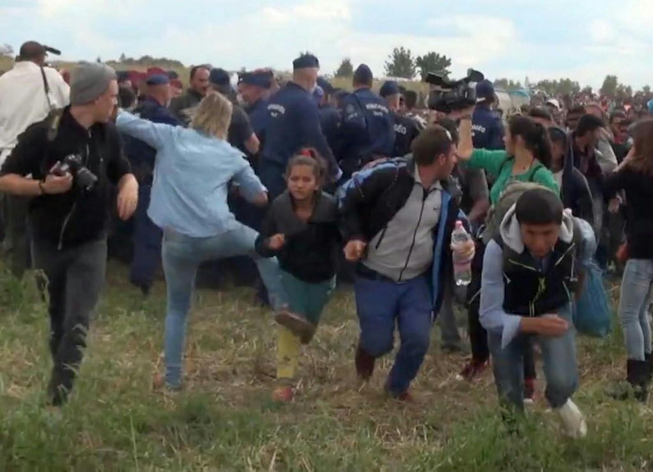 In this image taken from TV a Hungarian camerawoman, center left in blue, kicks out at a young migrant who had just crossed the border from Serbia near Roszke Hungary Tuesday Sept. 8, 2015. The camerawoman has been fired after she was caught on video kicking and tripping migrants entering Hungary across the border with Serbia. The N1TV Internet channel said their employee, widely identified in Hungarian media as Petra Laszlo, has been dismissed because she "behaved unacceptably" at a makeshift g