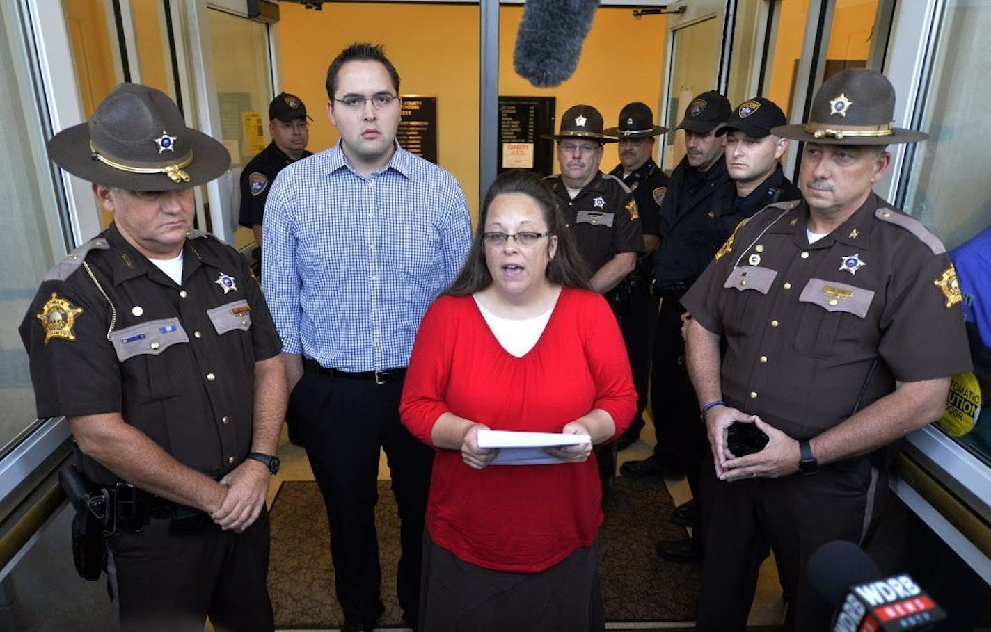 Surrounded by Rowan County Sheriff's deputies, Rowan County Clerk Kim Davis, center, with her son Nathan Davis standing by her side, makes a statement to the media at the front door of the Rowan County Judicial Center in Morehead, Ky., Monday, Sept. 14, 2015. Davis announced that her office will issue marriage licenses under order of a federal judge, but will not have her name or office listed.