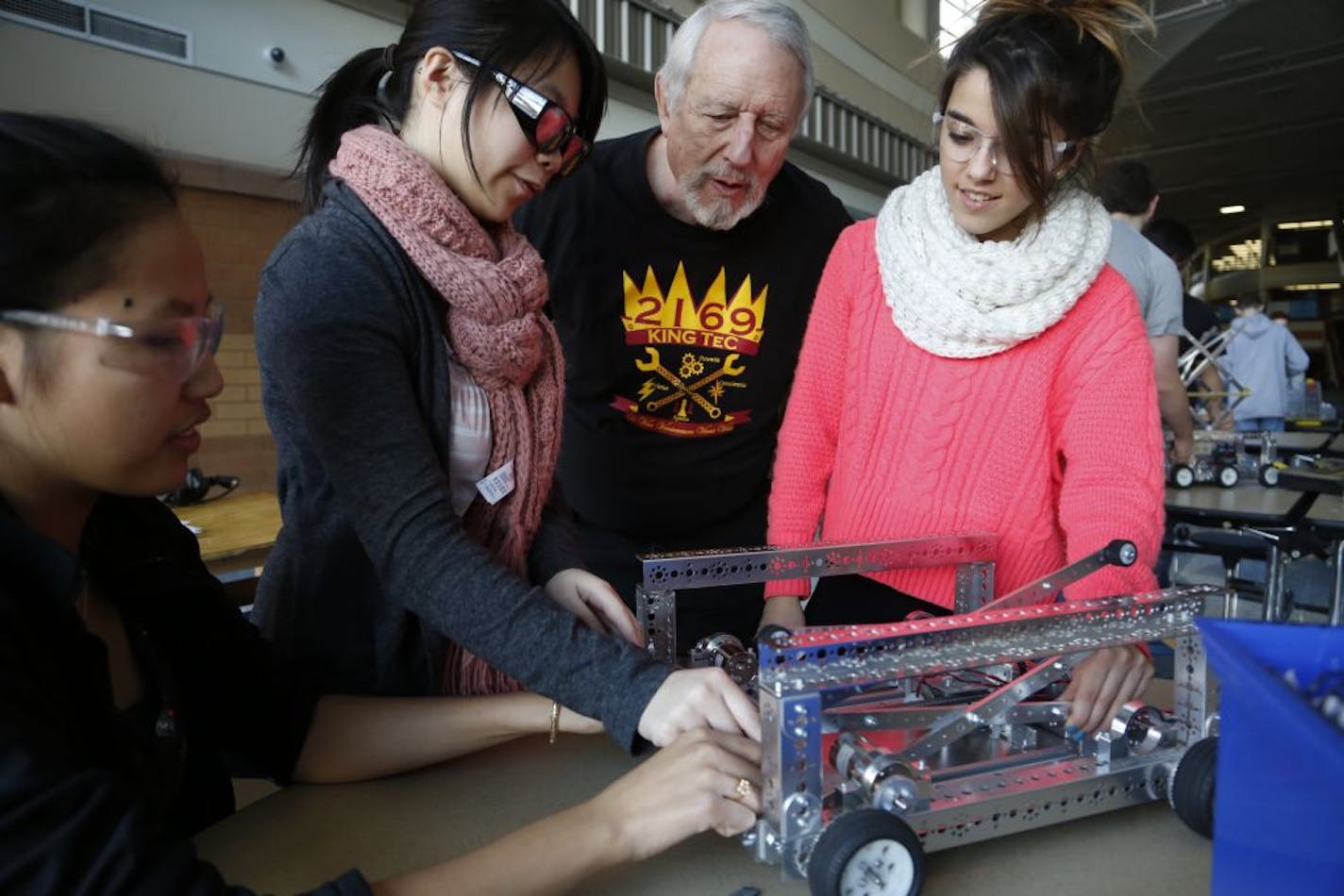 At Prior Lake H.S., Phillisha Cham, Cindi Chieu, and Lidia Gonzales, an exchange student from Spain get help with their robot from volunteer retired engineer, John Titus.