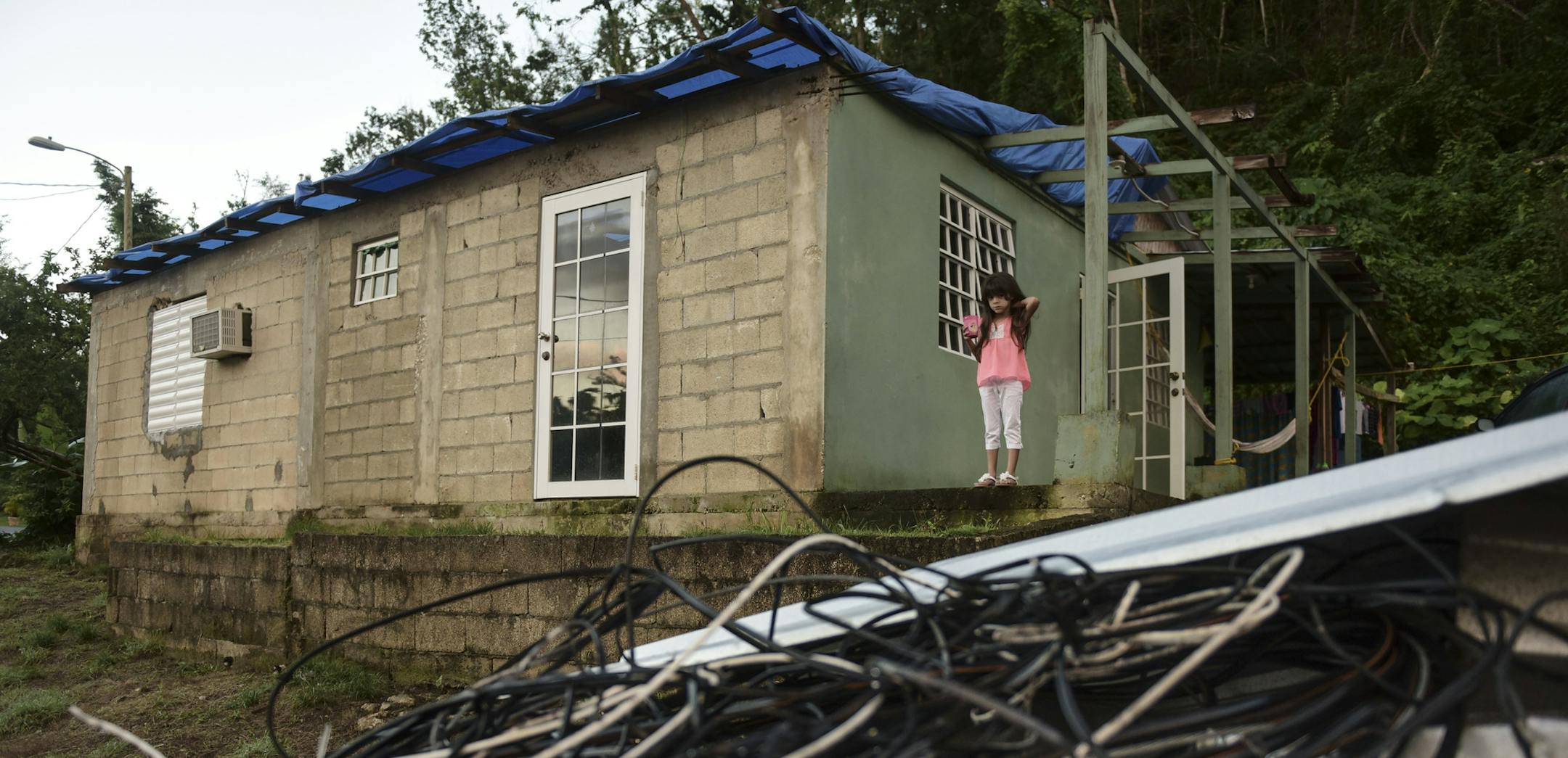 In this Dec. 22, 2017 photo, six year old Melanie Oliveras Gonz·lez stand on the porch of her house, in front of a handful of electric cables knocked down by the winds of Hurricane Maria, in Morovis, Puerto Rico. Morovis has been without power since hurricane smashed into the island in November. (AP Photo/Carlos Giusti)