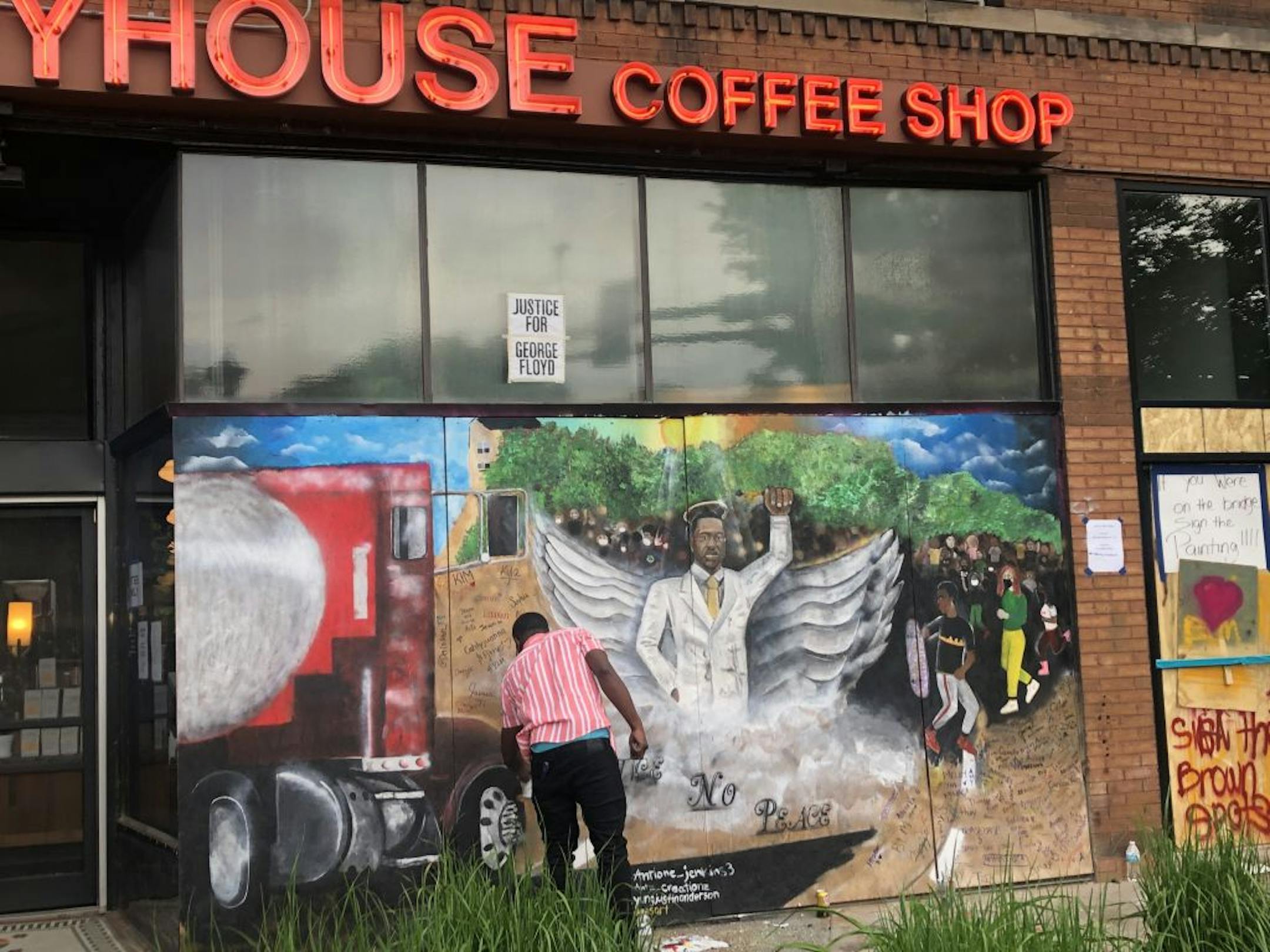 An artist paints a bright image of George Floyd in a white suit with angel wings and a halo on the side of Spyhouse coffee at 2404 Hennepin Ave S.