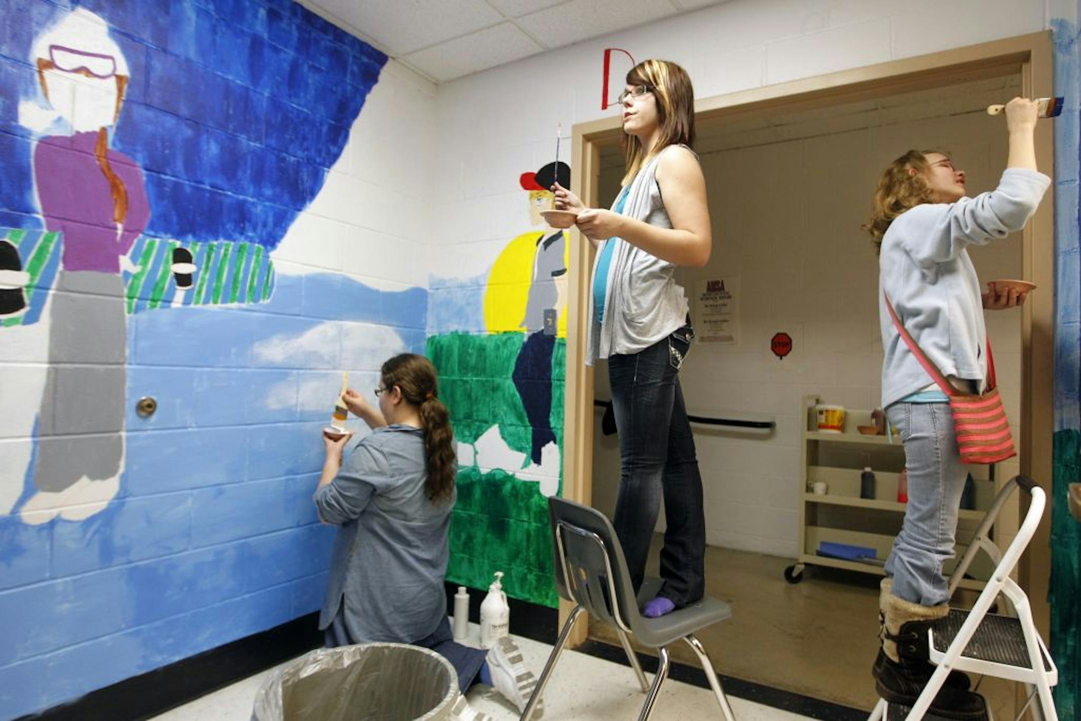 At Anoka Middle School for the Arts, Students Madeline Fragal, Bailey Hoffman, and Alissa Little are working on a four-seasons mural for a "Welcoming Spaces" program. The mural is intended to make a classroom inviting.