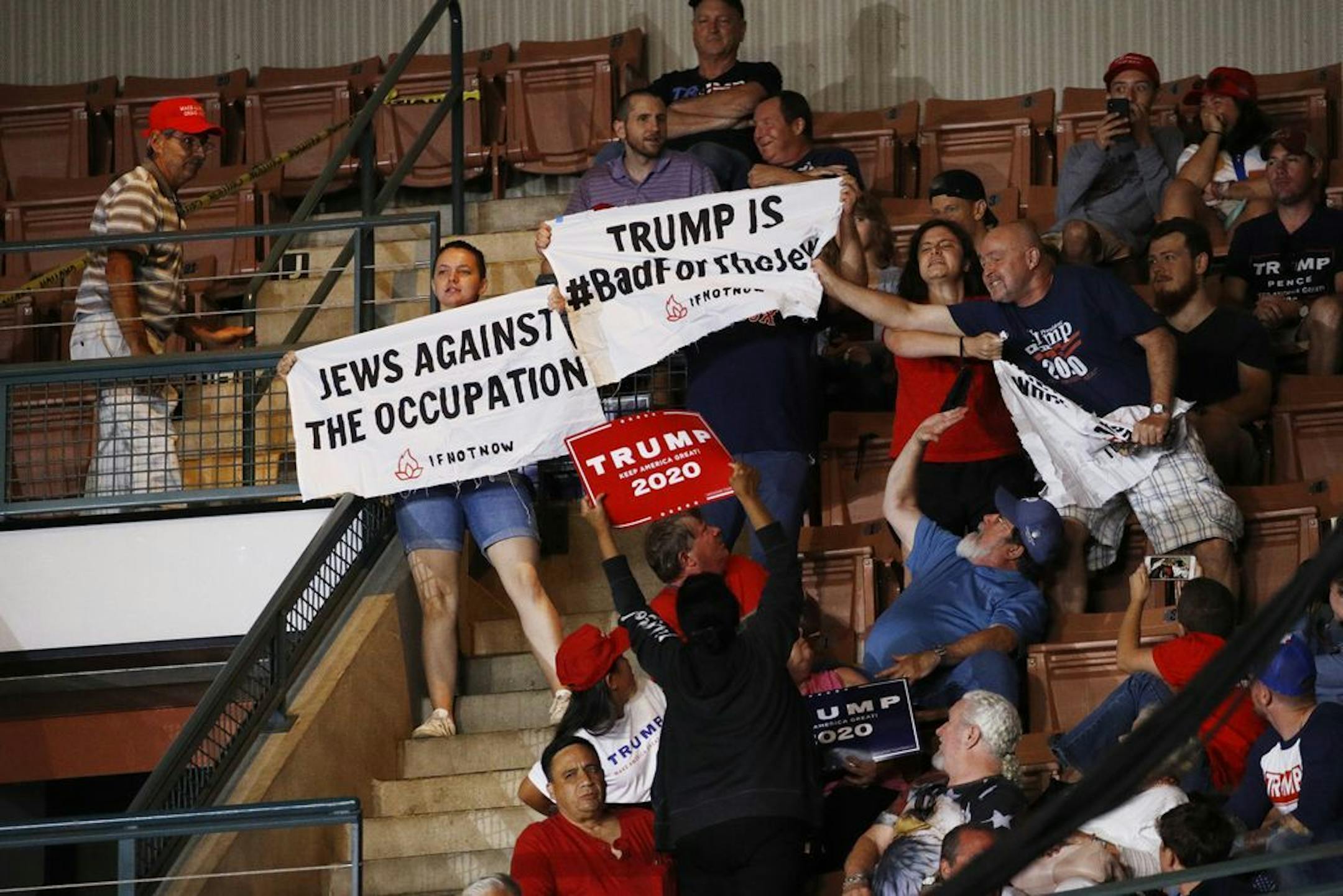 A Trump supporter, right, tries to grab a protesters' sign as President Donald Trump speaks at a campaign rally, Thursday, Aug. 15, 2019, in Manchester, N.H.