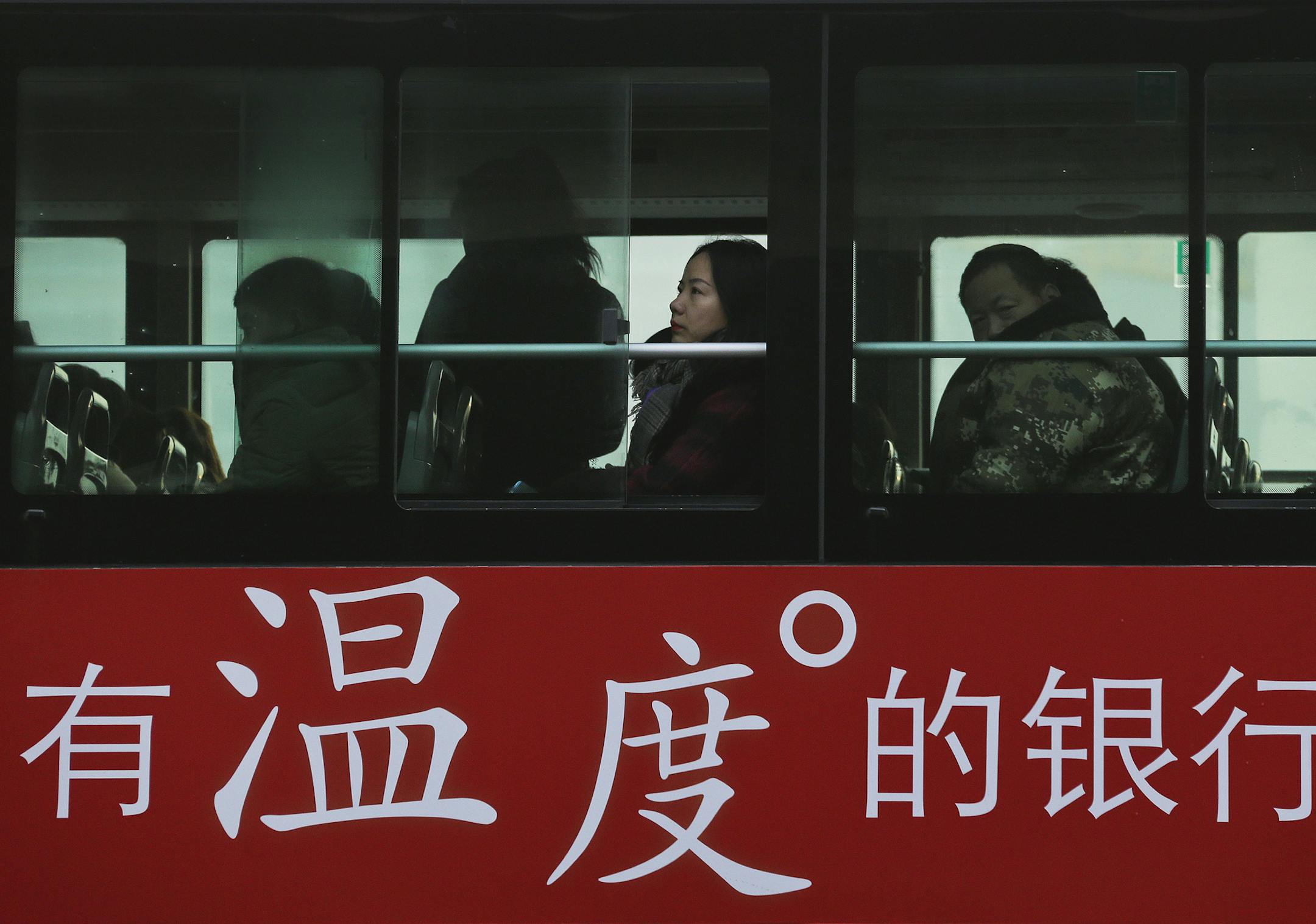 Commuters look out of a window of a bus with a bank advertise during the morning rush hour in Beijing, Tuesday, Nov. 13, 2018. The potential damage to global trade brought on by President Donald Trump's tariffs battle with Beijing is looming as leaders of Southeast Asian nations, China, the U.S. and other regional economies meet in Singapore this week. The advertisement reads "A warm-hearted bank." (AP Photo/Andy Wong) ORG XMIT: XAW101