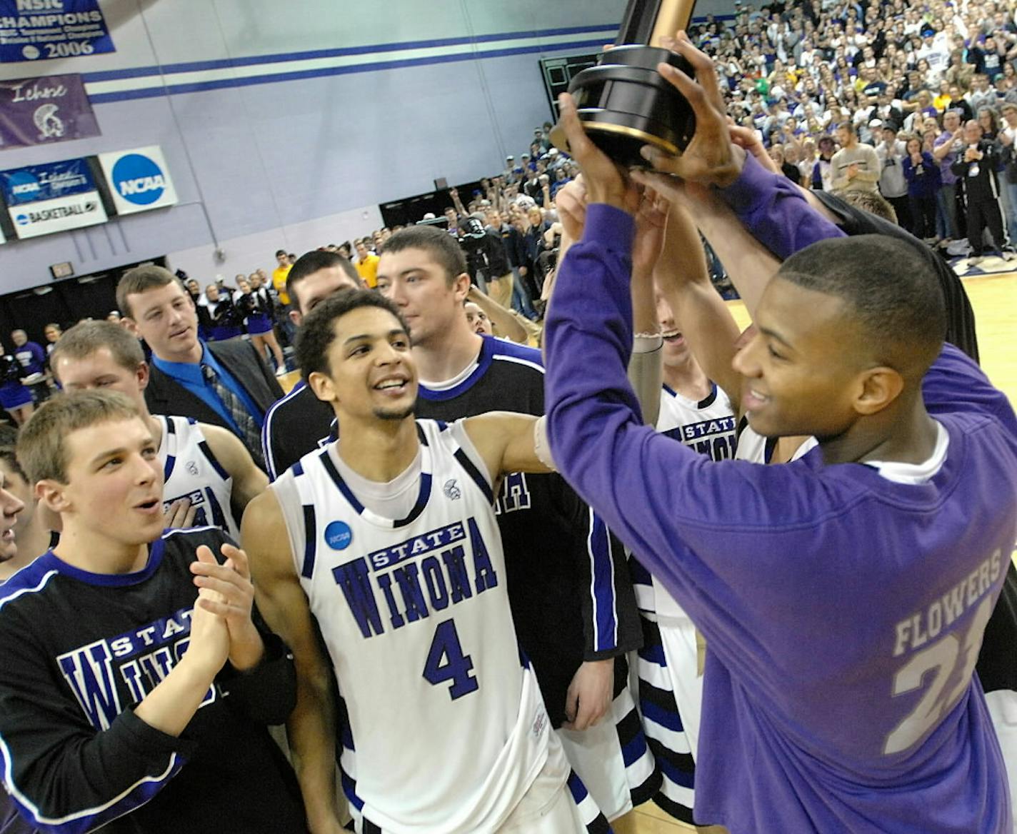 Winona State's Brad Meyer, left, applauds as Quincy Henderson (4) and Jonte Flowers, right, hold up the NCAA Division II North Central Region championship trophy following the Warriors' 68-60 win over Northern State,