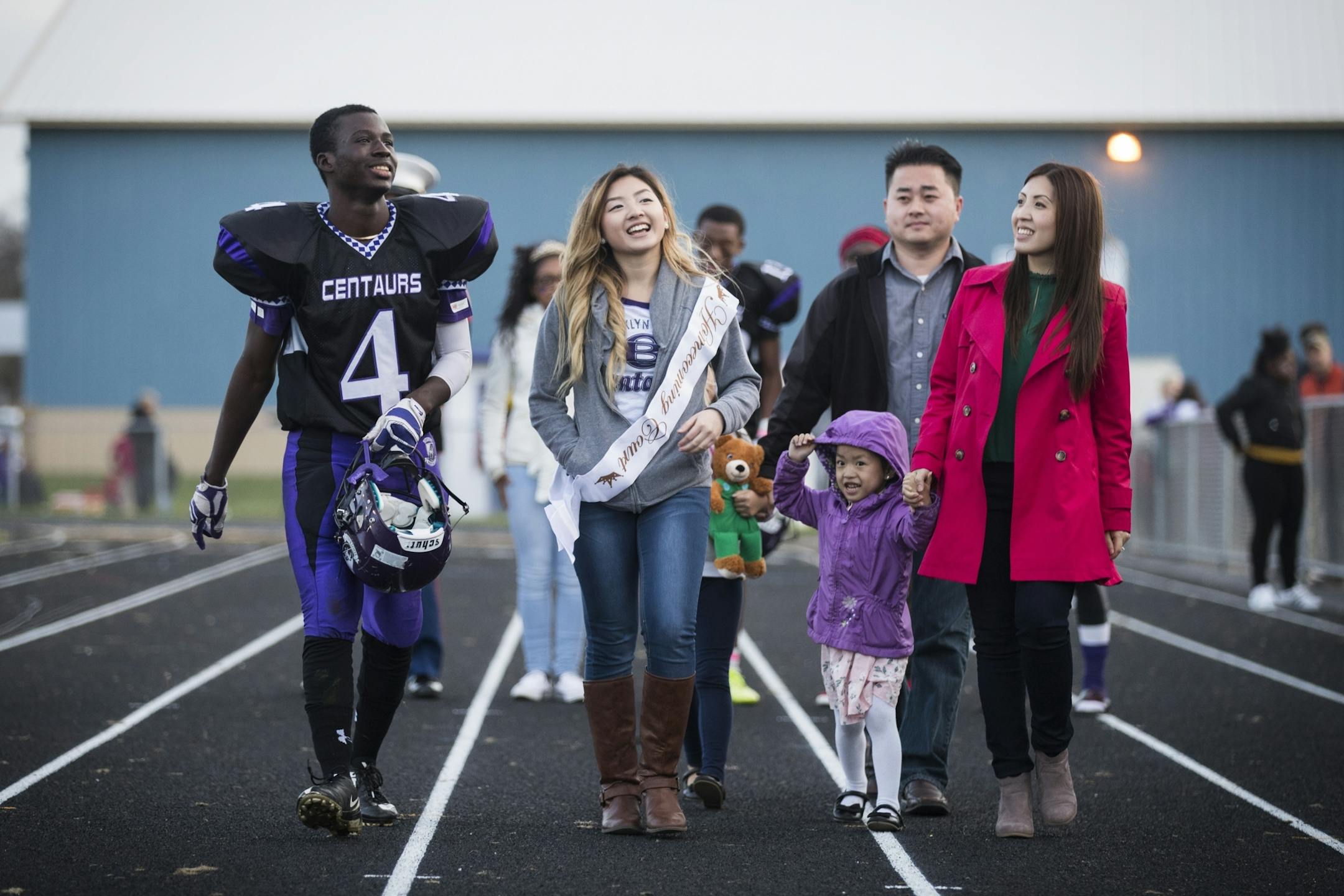 Homecoming court members Molubah Seley, from left, Jade Yang walk with Jade's family during the Brooklyn Center High School homecoming football game. From right is Jade's mother Zoua Her, father Chia Yang and sister Ivy, 3.