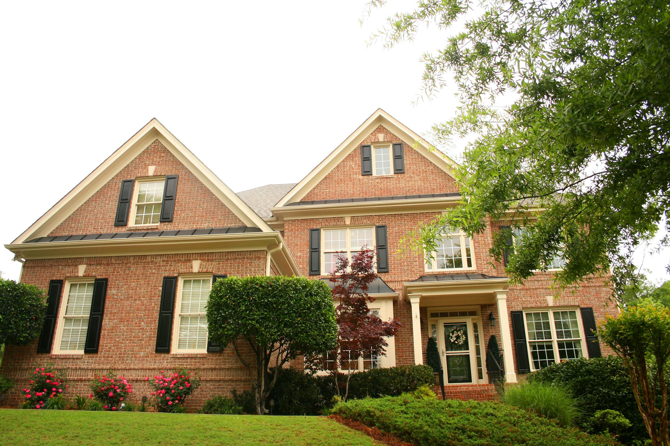 Brick house with small portico in front and dark shutters.