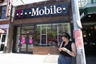 FILE -- A woman checks her smartphone outside a T-Mobile store in New York on June 11, 2019. The Justice Department on Friday, July 26, 2019, approved
