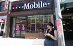 FILE -- A woman checks her smartphone outside a T-Mobile store in New York on June 11, 2019. The Justice Department on Friday, July 26, 2019, approved