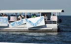 In this Saturday, July 8, 2017, photo provided by Mille Lacs Messenger, people on a boat encircle Minnesota Gov. Mark Dayton, not pictured, on Mille L