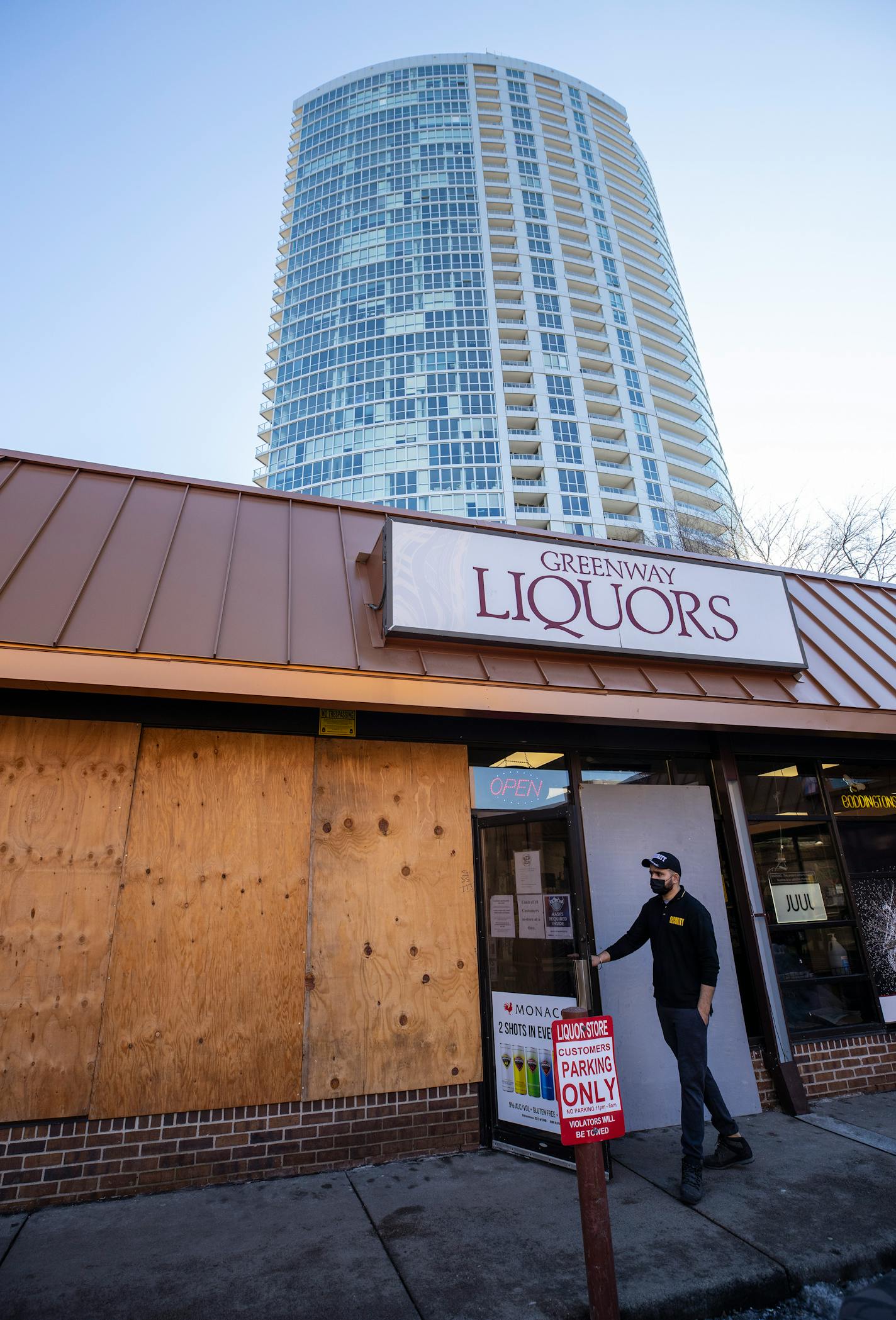 A security guard opened up the door for a customer at Greenway Liquors. Greenway Liquors is leaving up its boards during the trial of Derek Chauvin.