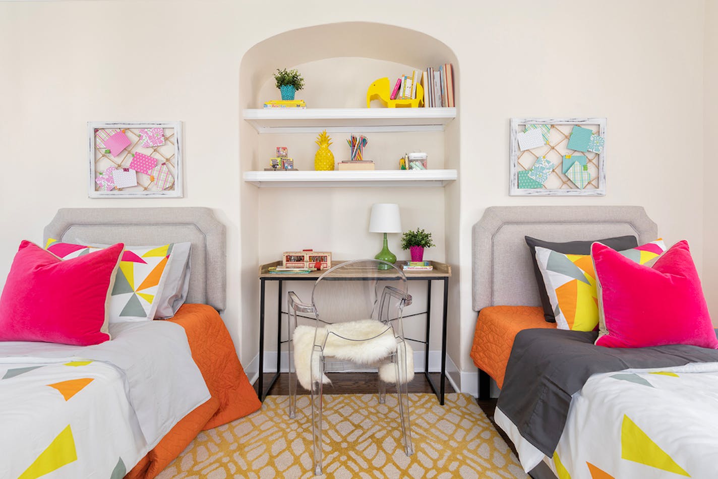 Dorm room with two twin beds with colorful pillows and tack boards above each bed. In between is a wall nook with shelving used as a bookcase.