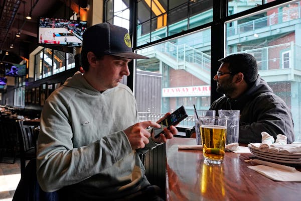 Taylor Foehl, left, of Boston looked at a mobile betting app on his phone after placing a wager while watching a men’s college basketball game at th