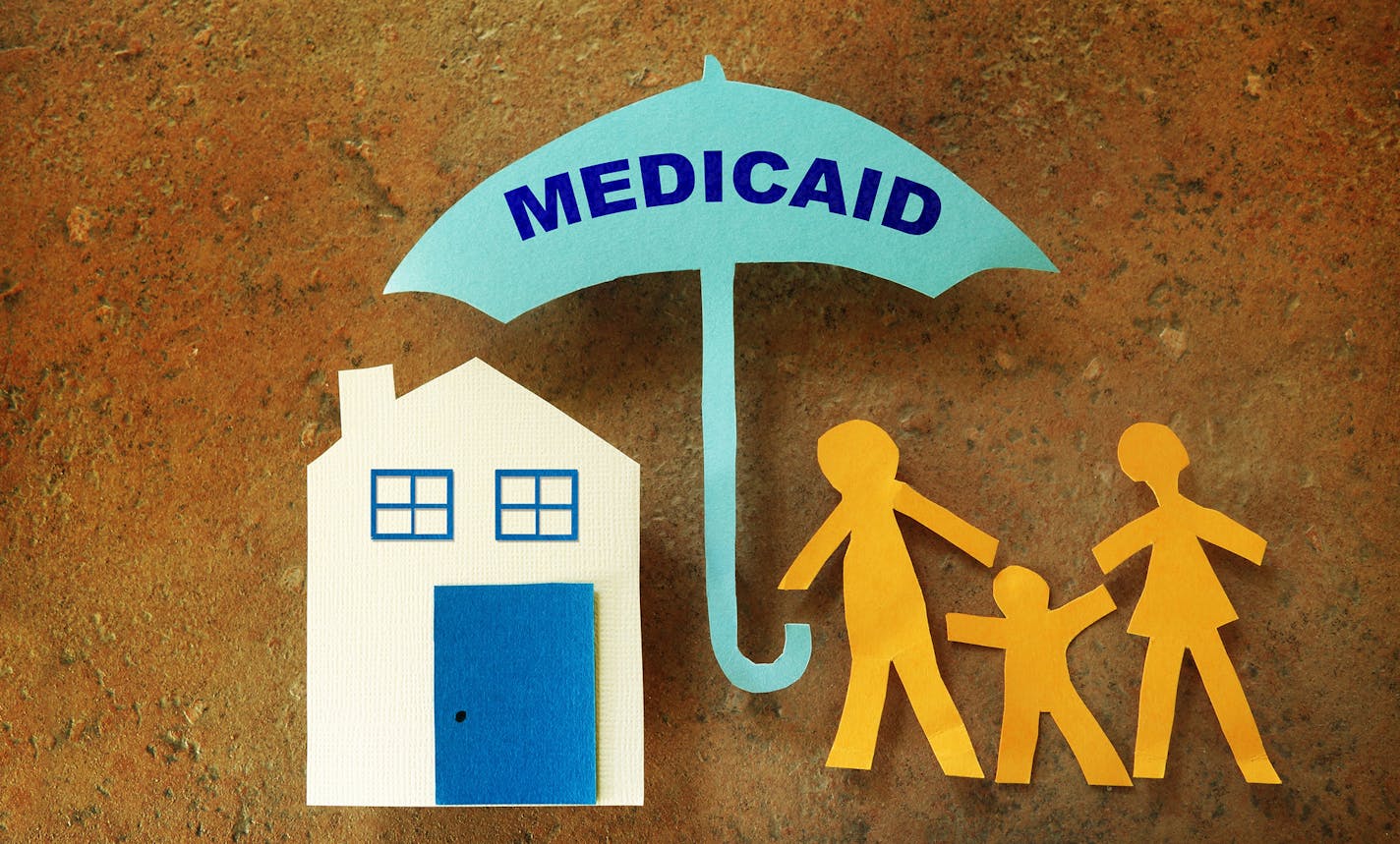 iStock
Paper cutout family with house under a Medicaid umbrella.