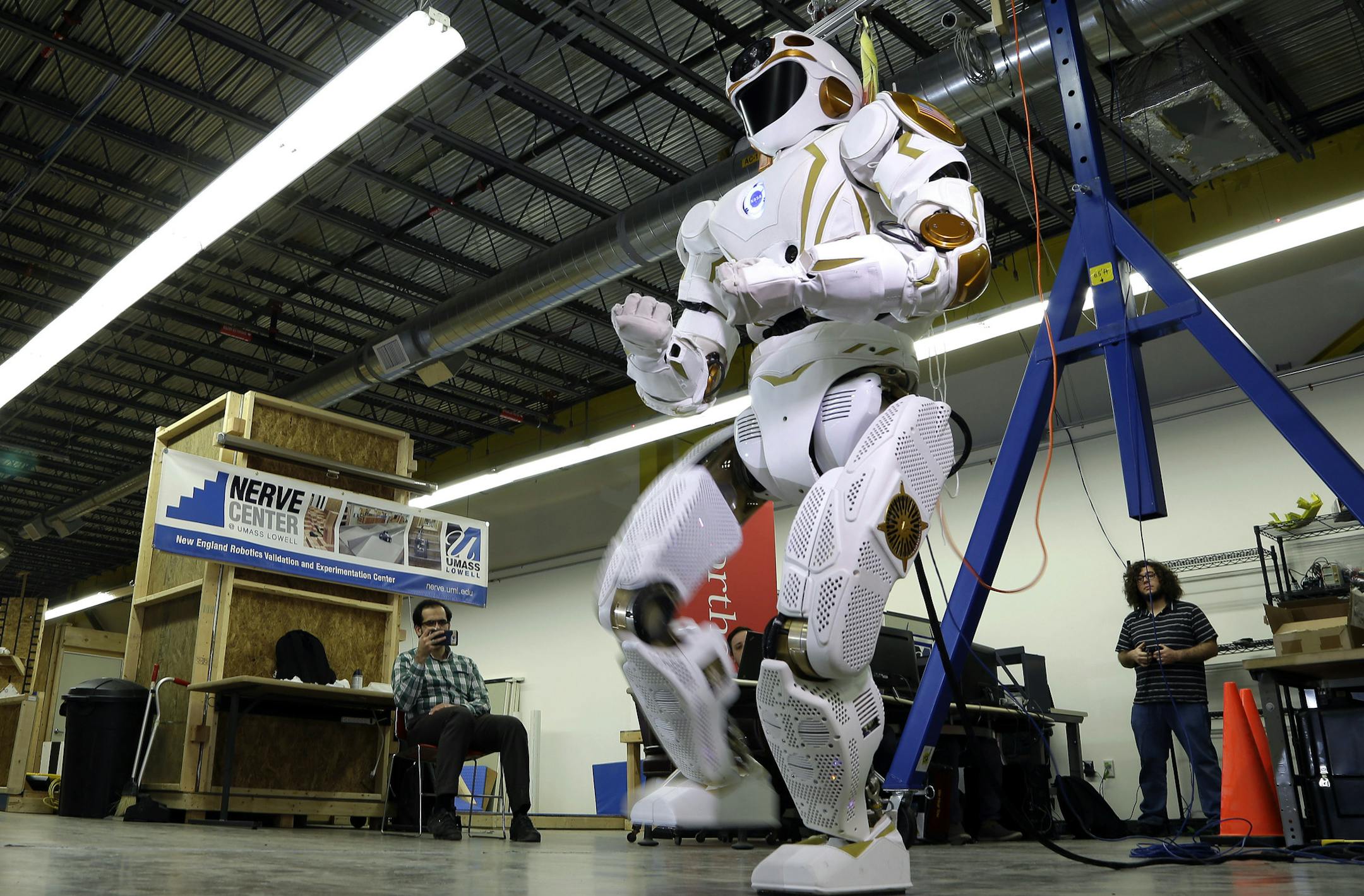 In this May 2, 2016 photo, researchers watch a six-foot-tall, 300-pound Valkyrie robot walk slowly at University of Massachusetts-Lowell's robotics center in Lowell, Mass. "Val," one of four sister robots built by NASA, could be the vanguard for the colonization of Mars by helping to set up a habitat for future human explorers. NASA spokesman Jay Bolden says the agency aims to get to Mars by 2035 and it’ll be the Valkyries or their descendants paving the way. (AP Photo/Elise Amendola)