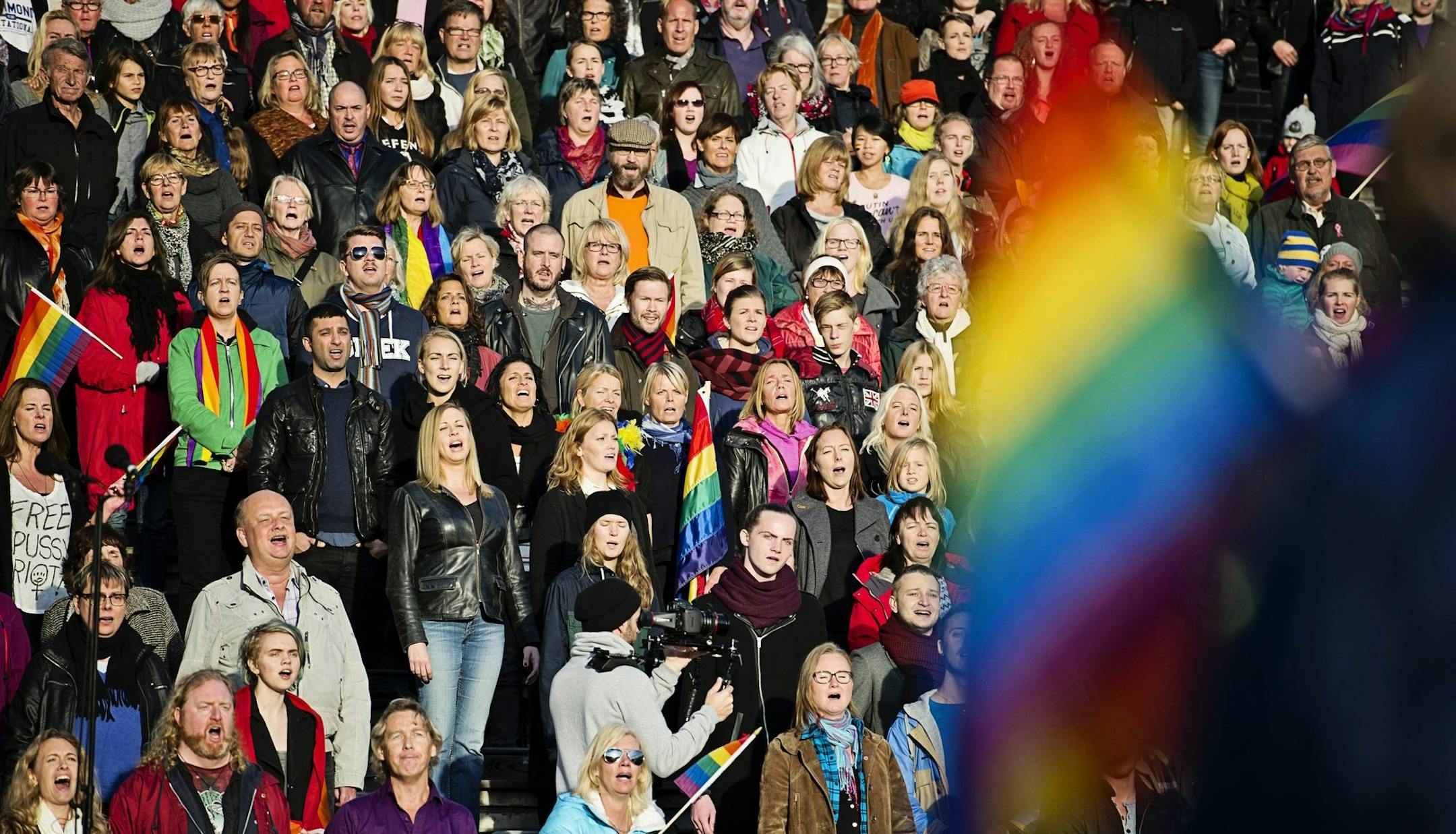 A crowd of people sing the Russian National Anthem, at the Stockholm Olympic Stadium on Sunday Oct. 6, 2013, while raising rainbow flags in solidarity with the Russian lesbian, gay, bisexual and transgender (LGBT) community. A project called 'Live and Let Love' is expected to use footage from the event to be cut together with other singers and musicians from around the world to make a video film that will be shown on YouTube ahead of the Olympic games in Sochi. (AP Photo/TT News Agency/Erik Mart