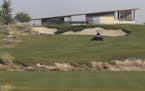 In this Tuesday, Dec. 20, 2016 photo, an employee mows the grass in front of the clubhouse at the Trump International Golf Club, in Dubai, United Arab