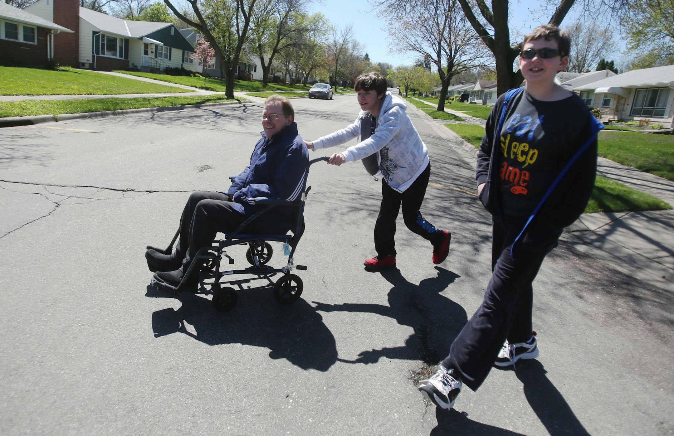 With his limbs having atrophied by A.L.S. walking distances is all but impossible. Bob White gets a ride into the neighborhood with the help of his son Kieran, 13, who is joined by his neighborhood friend Connor Nicolay, 13, Friday, April 29, 2016, in West St. Paul, MN.](DAVID JOLES/STARTRIBUNE)djoles@startribune Each day, an estimated 30,000 to 40,000 children across Minnesota provide care to someone in their family who is physically or mentally disabled and is too debilitated to care for thems