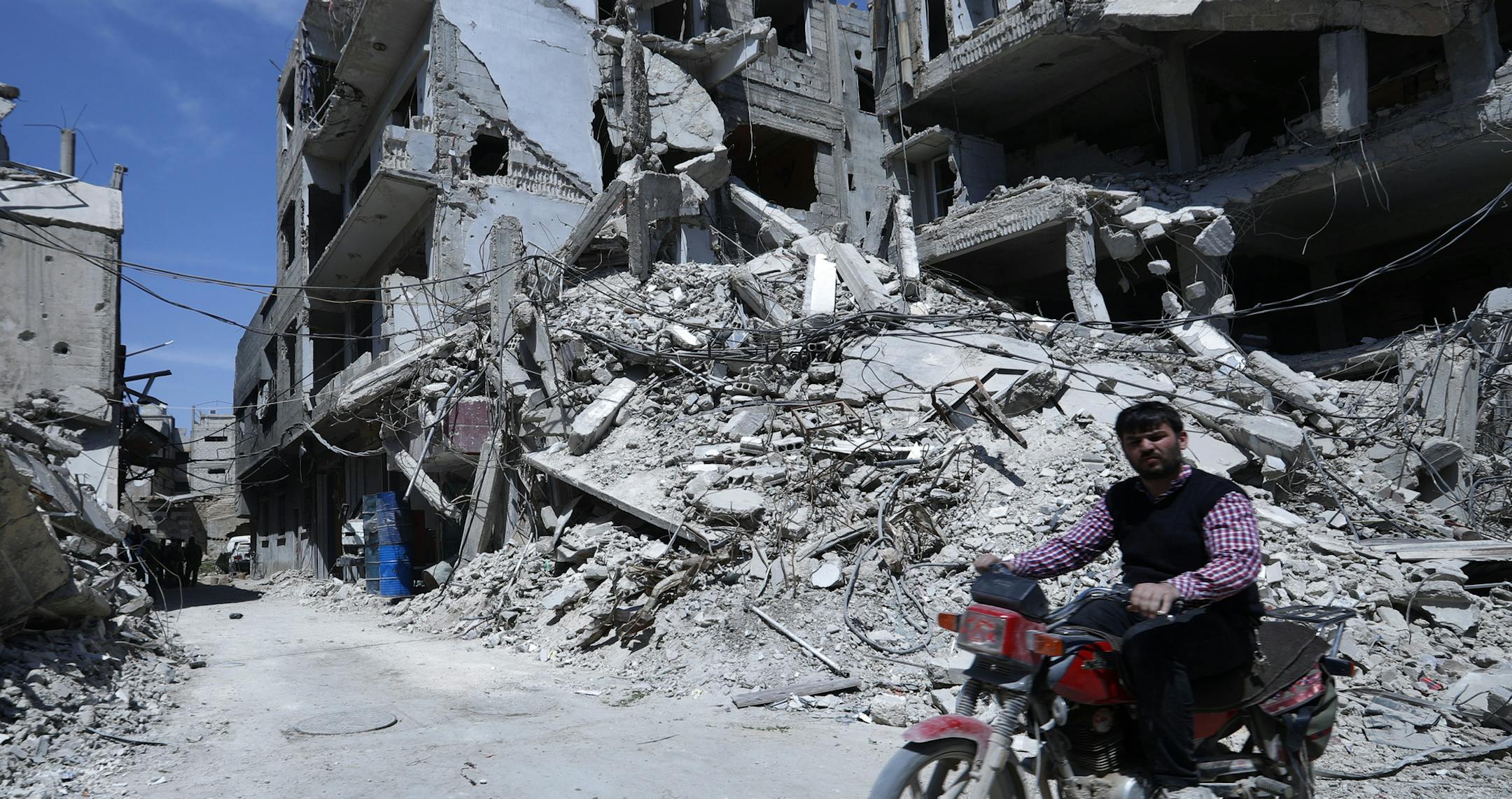 A man rides past destruction in the town of Douma, the site of a suspected chemical weapons attack, near Damascus, Syria, Monday, April 16, 2018. Faisal Mekdad, Syria's deputy foreign minister, said on Monday that his country is "fully ready" to cooperate with the fact-finding mission from the Organization for the Prohibition of Chemical Weapons that's in Syria to investigate the alleged chemical attack that triggered U.S.-led airstrikes. (AP Photo/Hassan Ammar)