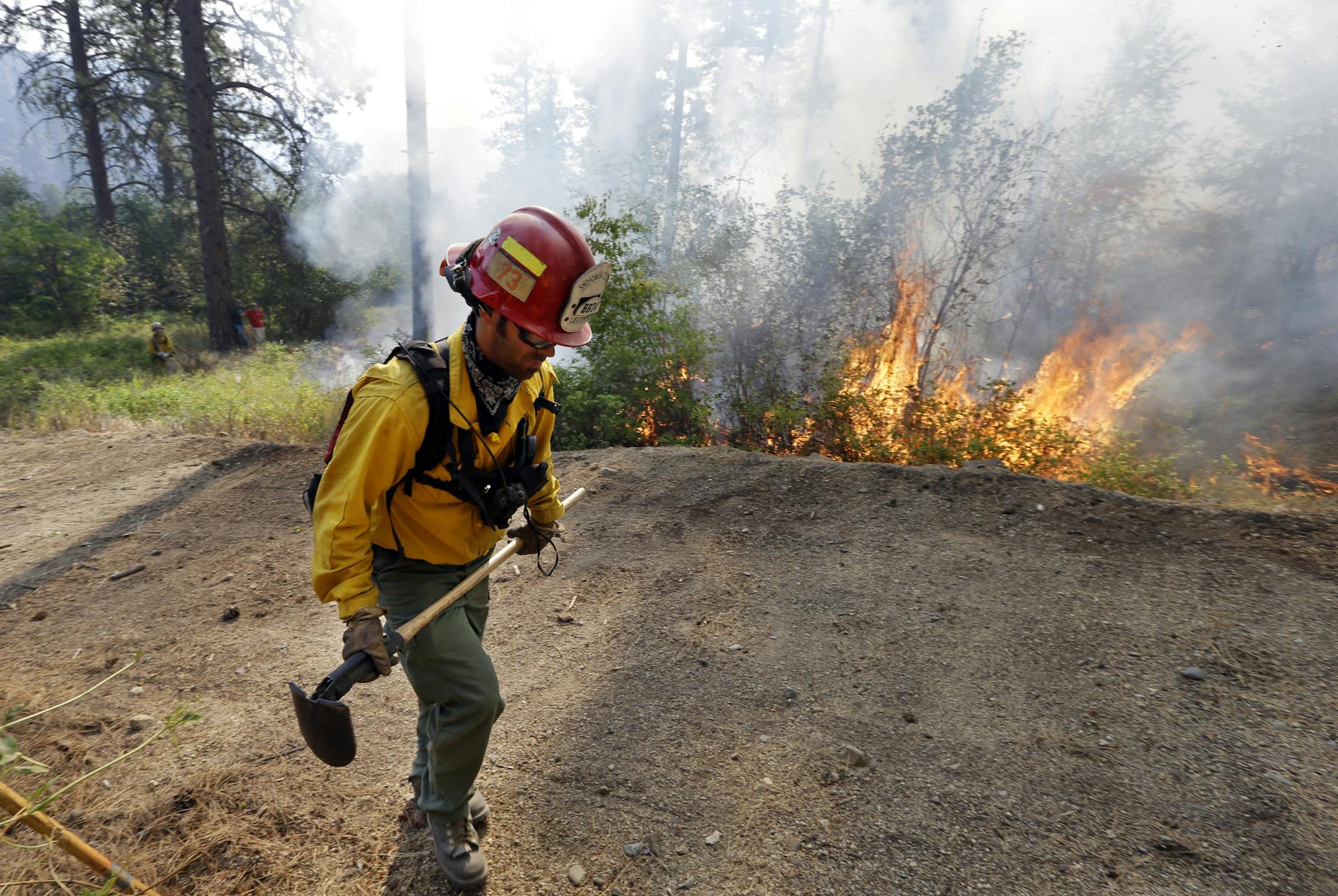 Firefighter Lt. Brandon Gardner walks along a driveway being used as a fire break next to a fire being used to burn out an area between houses and the main fire Saturday, Aug. 22, 2015, in Okanogan, Wash. Reduced winds on Saturday helped firefighters gain the upper hand against a series of giant wildfires in north-central Washington that earlier left three firefighters dead. (AP Photo/Elaine Thompson)