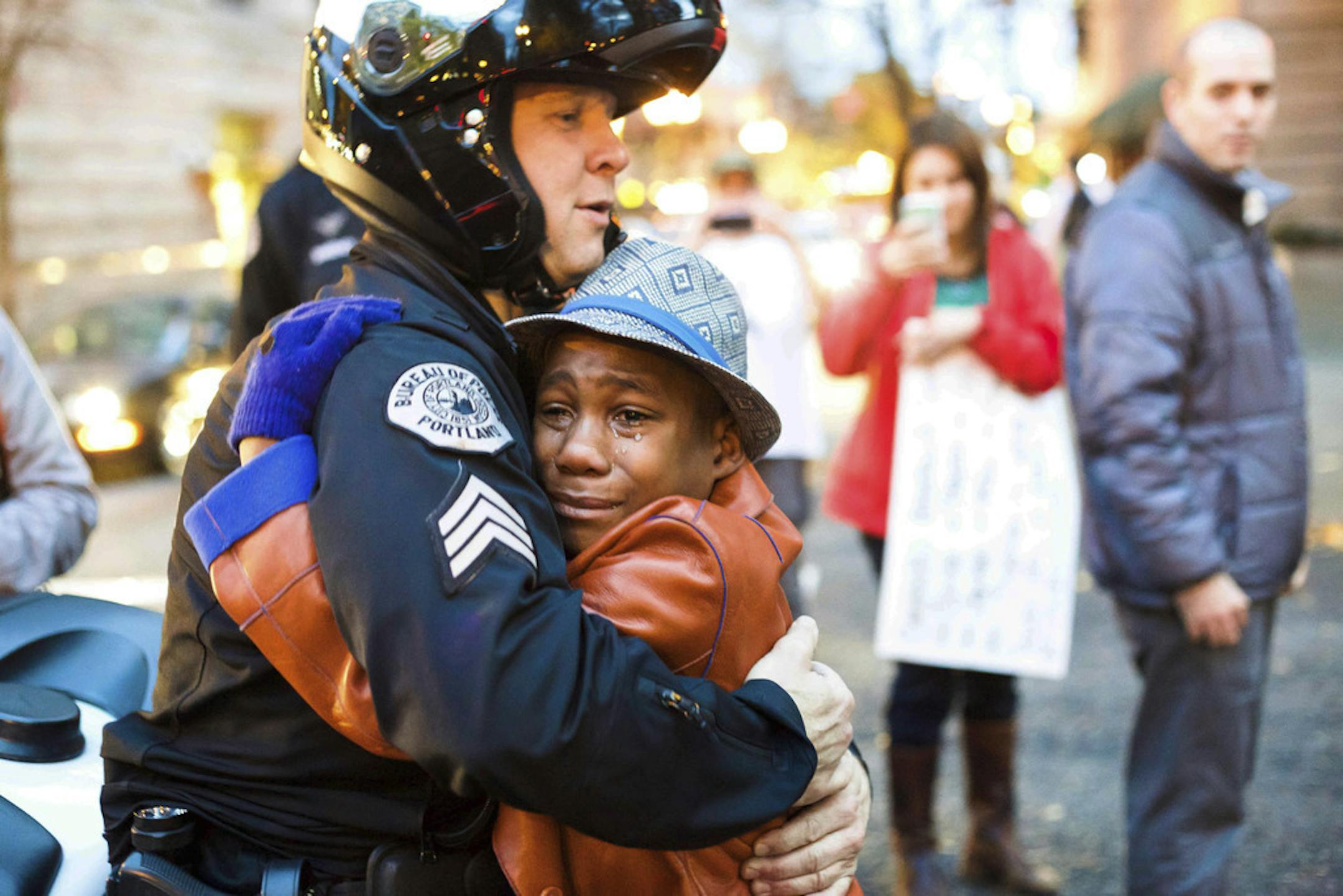 FILE - In this Nov. 25, 2014, file photo provided by Johnny Nguyen, Portland police Sgt. Bret Barnum, left, and Devonte Hart, 12, hug at a rally in Portland, Ore., where people had gathered in support of the protests in Ferguson, Mo. Authorities have said two women and three children were killed Monday, March 26, 2018, when their SUV fell from a cliff along Pacific Coast Highway in Mendocino County. Hart is one of the three other children still missing after the vehicle fell off a cliff. He had