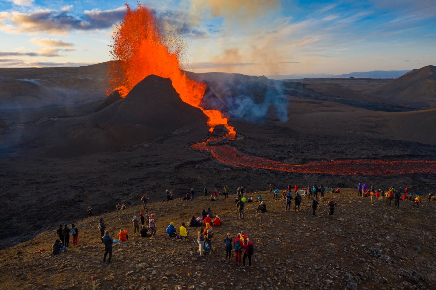 People watch as lava flows from an eruption from the Fagradalsfjall volcano on the Reykjanes Peninsula in southwestern Iceland on Tuesday, May 11, 2021. The glow from the bubbling hot lava spewing out of the Fagradalsfjall volcano can be seen from the outskirts of Iceland's capital, Reykjavík, which is about 32 kilometers (20 miles) away. Pandemic or no pandemic, the world will never stand still. That's perhaps no clearer than in Iceland where the Fagradalsfjall volcano has awoken from a slumber that has lasted 6,000 years, give or take a year or two.