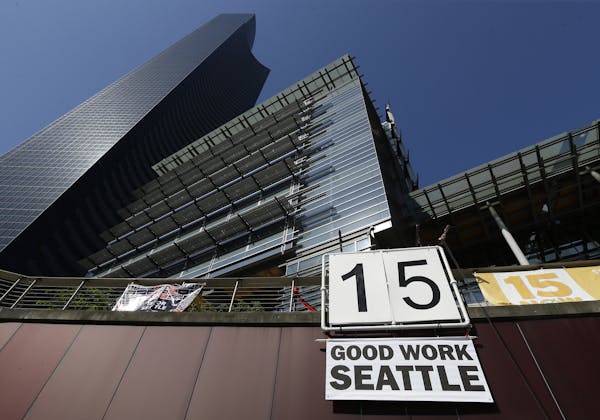 FILE - In this June 2, 2014, file photo, a sign that reads "15 Good Work Seattle" is displayed below Seattle City Hall, right, and the Columbia Center