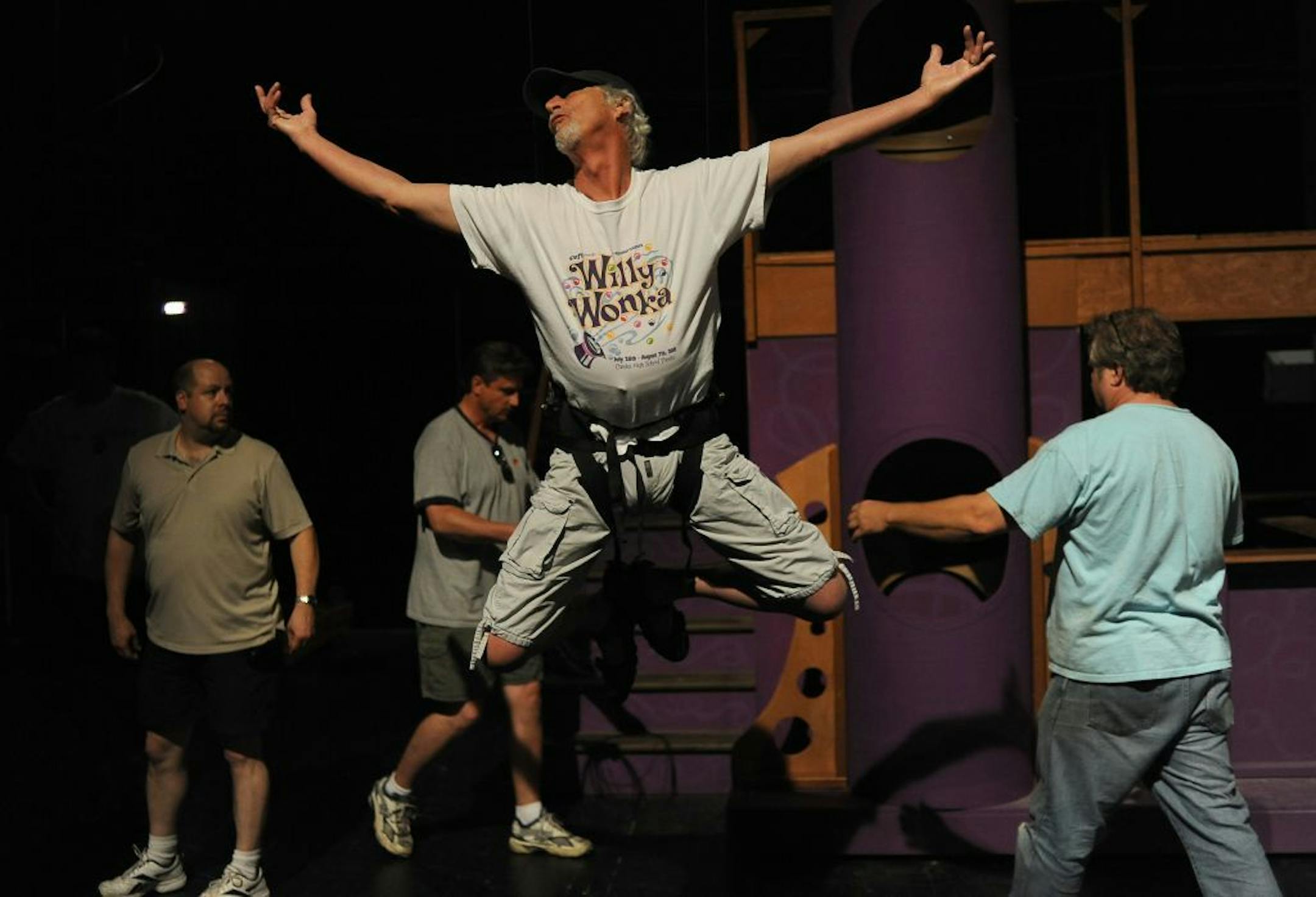 Charlie Title had some fun while practicing with his aerial harness, aided by scenic designer Randy Herget, right. Title, who plays Grandpa Joe in "Willy Wonka," had never done aerobatics in a show before, but said "once you get up there it's fun" and "exhilarating."
