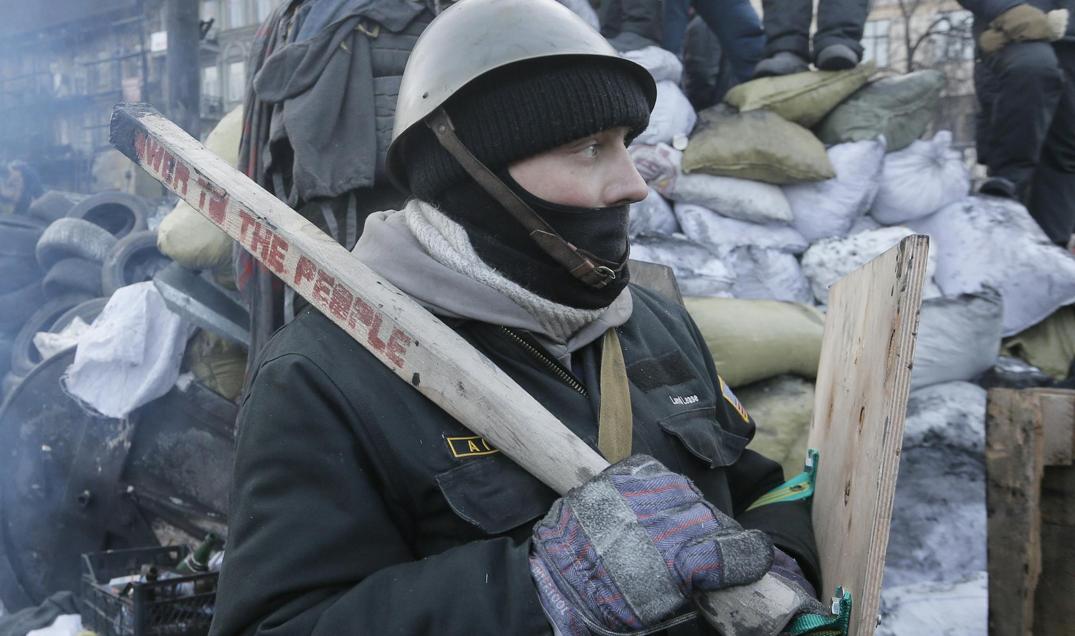 A protester stands guard at the barricades in front of riot police in Kiev, Ukraine, Monday, Jan. 27, 2014. Ukraine's justice minister is threatening to call for a state of emergency unless protesters leave her ministry building, which they occupied during the night. The seizure of the building early Monday underlined how anti-government demonstrators are increasingly willing to take dramatic action as they push for the president's resignation and other concessions. Protesters now occupy four si