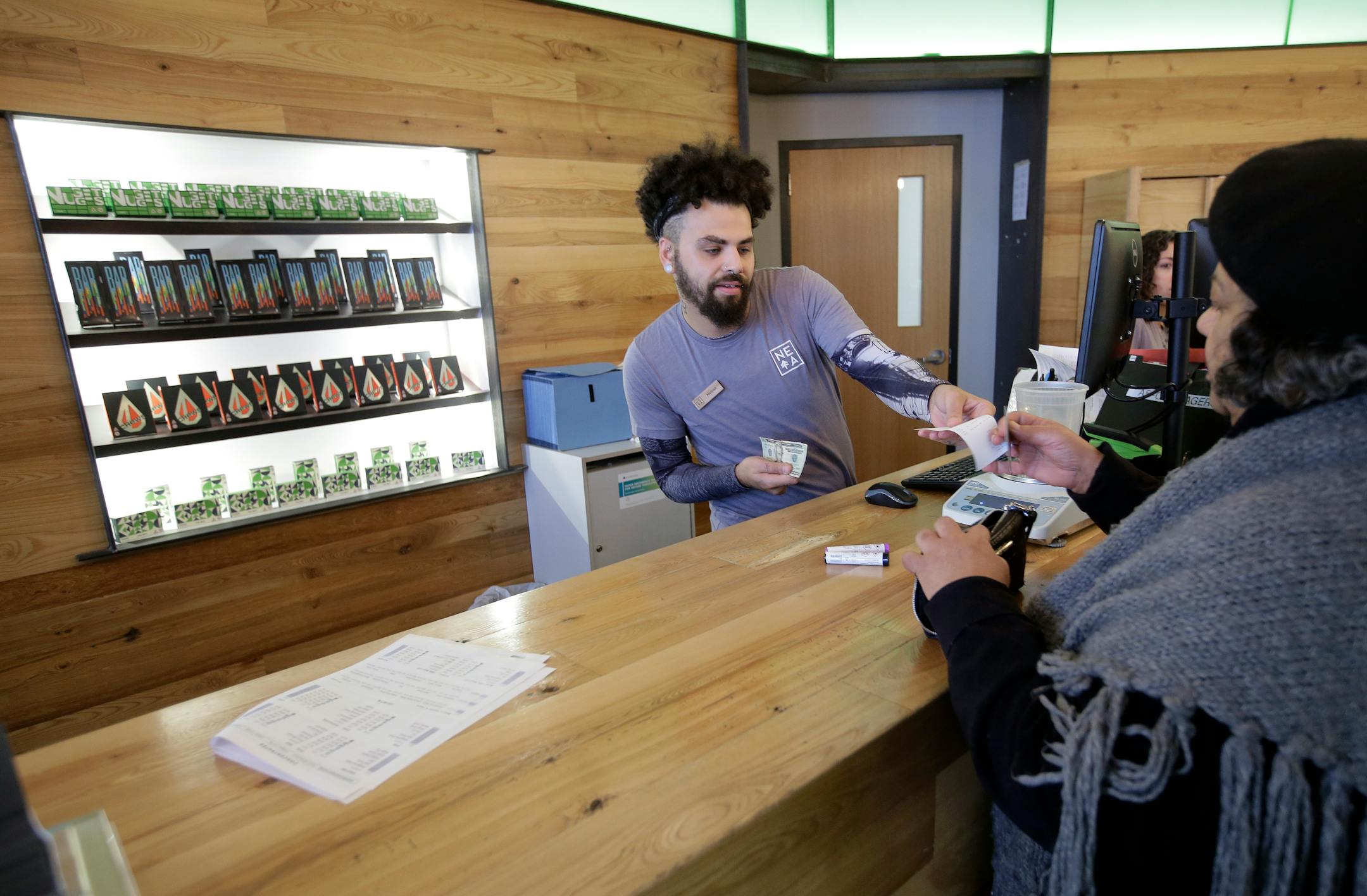 In this Wednesday, Oct. 17, 2018 photo patient service associate Nelson Rivera III, left, sells medical cannabis products to Victoria Silva, of Amherst, Mass., right, at a New England Treatment Access medical marijuana dispensary, in Northampton, Mass. Within days perhaps, the medical marijuana dispensary in Northampton expects to receive the final go-ahead to throw its doors open to anyone 21 or older who wants to purchase cannabis products ranging from flower to edibles, creams and even suppos