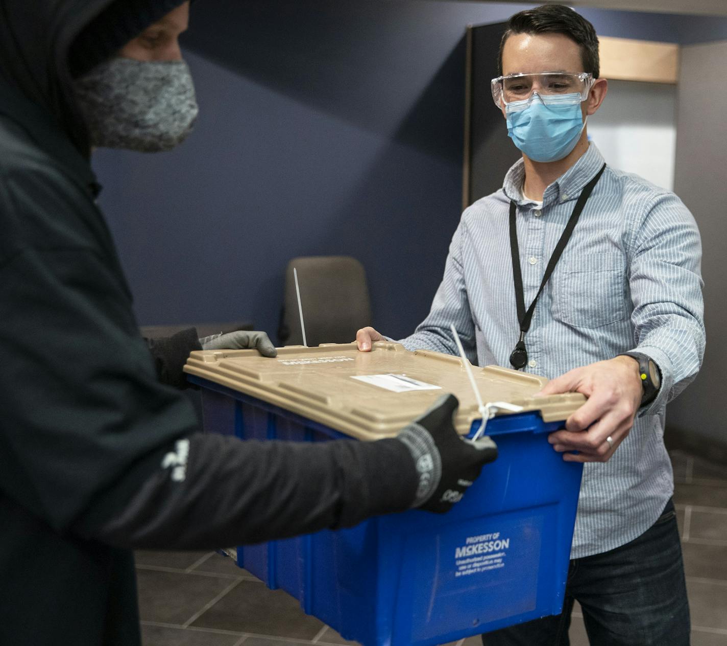 Teague Alexy, left, a courier for Dash Express, handed off cases of medication to Mike Krussow, a medication access representative for Sawtooth Mountain Clinic in Grand Marais, a town without an independent, full-service pharmacy.