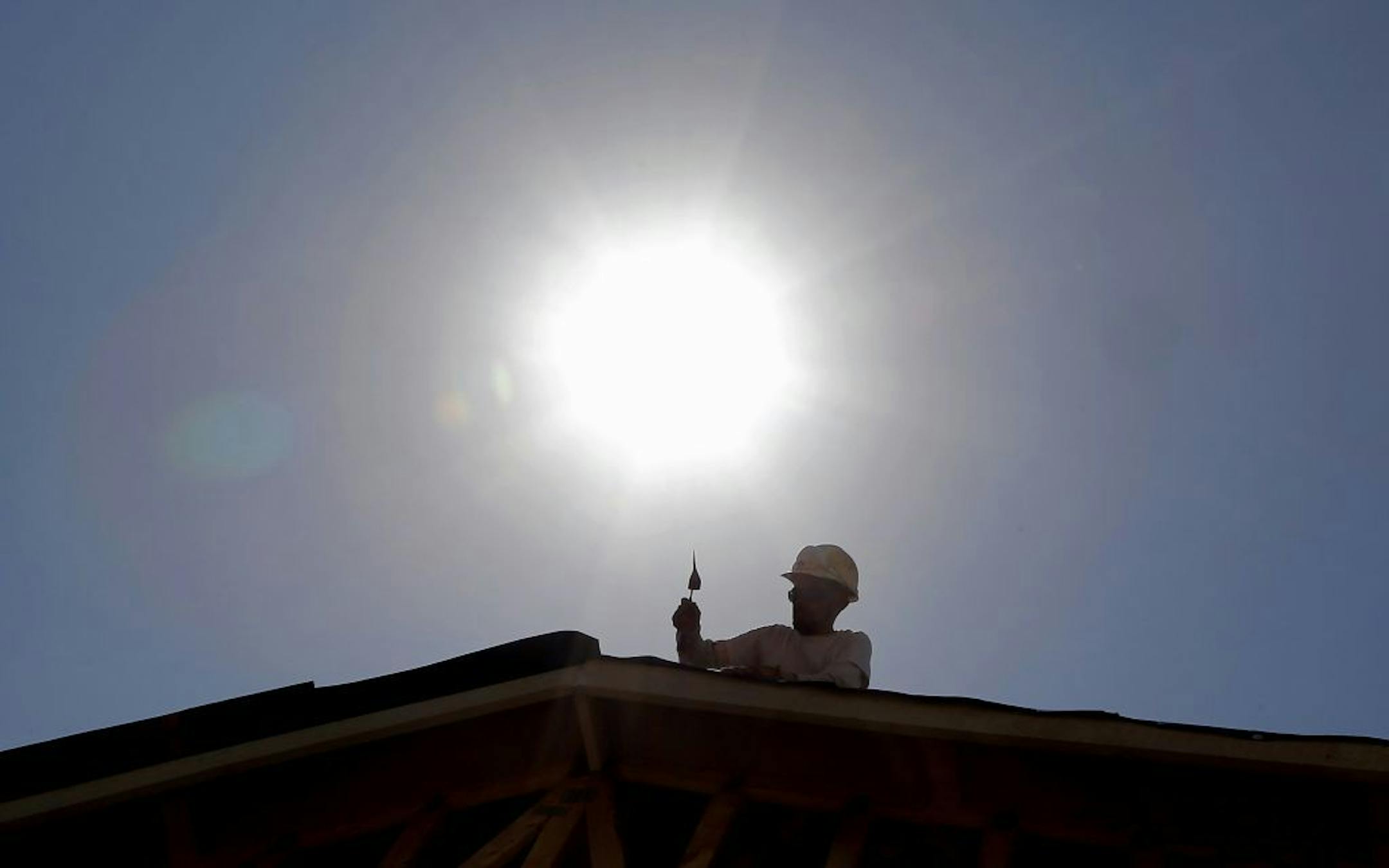 FILE - In this July 25, 2014, file photo, a roofer works under the midday sun in Gilbert, Ariz. Hotter days mean less cold cash for Americans, according to a new study matching 40 years of temperatures to economics. Days that averaged about 77 degrees ended up reducing people�s income by about $5 a day, when compared to days that were about 20 degrees cooler. A county�s average economic productivity decreases by nearly 1 percent for every degree Fahrenheit that the average daily temperature is a