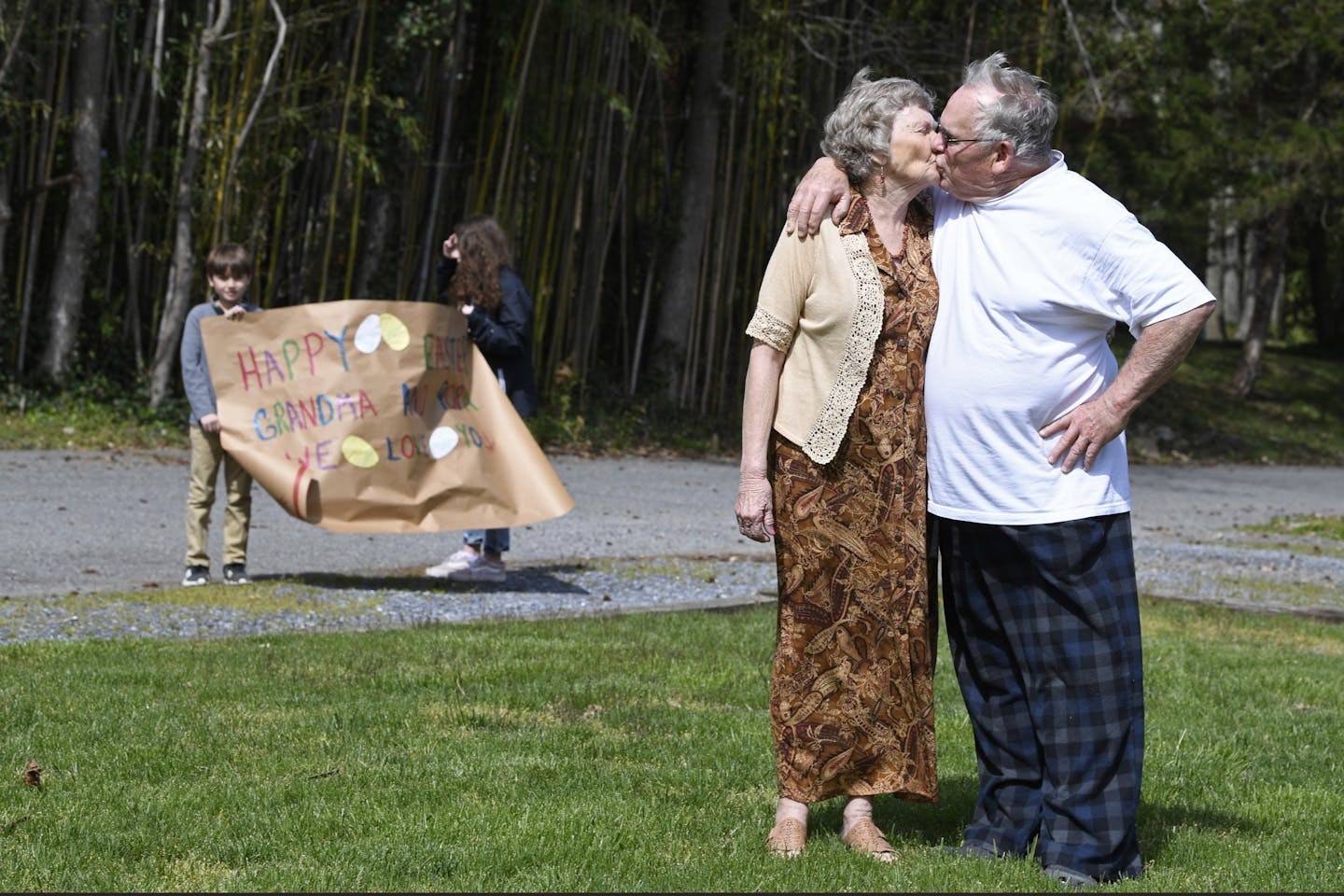 Sharon and Bart Williams kiss as their grandchildren Mason Keen, 9, left, and Rowan Keen, 14, second from left, hold a sign during a surprise stop by the Williams' home in Annapolis, Md., Sunday, April 12, 2020. Family and friends surprised the Williams' for a social distancing celebration of their 56th wedding anniversary. Because of the coronavirus, the Williams have stayed home to self-isolate and were surprised by the unexpected marking their anniversary