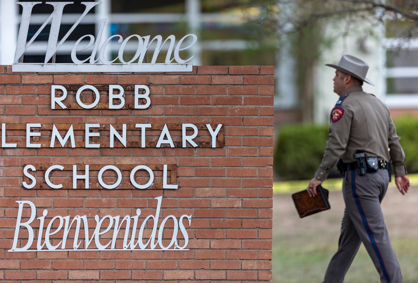 A state trooper walks past the Robb Elementary School sign in Uvalde, Texas, Tuesday, May 24, 2022, following a deadly shooting at the school. (William Luther/The San Antonio Express-News via AP)