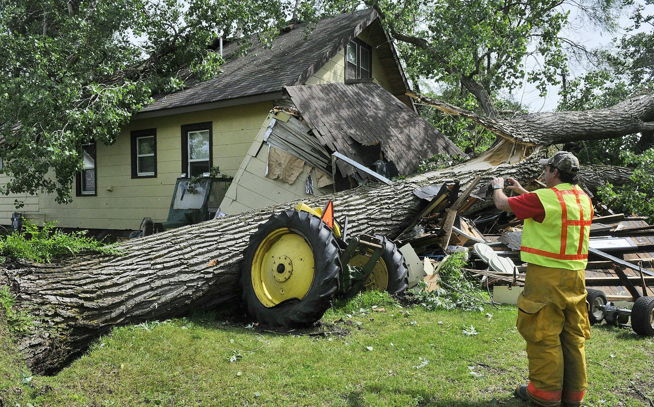 ADVANCE FOR MONDAY, SEPT 9 - FILE - In this June 21, 2013 file photo, Fire Chief Rodney Schaefer stops to take a photo of a downed tree on a home and antique tractor in Rockville, Minn. after a strong overnight storm caused damage over much of central Minnesota. Minnesota legislative leaders will hold a special session on Sept. 9 to provide relief to Minnesota areas hit hard by June 2013 storms. Two lawmakers argue that the expense of such special sessions could be defrayed with the creation of