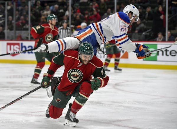 Edmonton Oilers' Benoit Pouliot flies over the top of Minnesota Wild's defenseman Marco Scandella, bottom, during the second period of an NHL hockey g