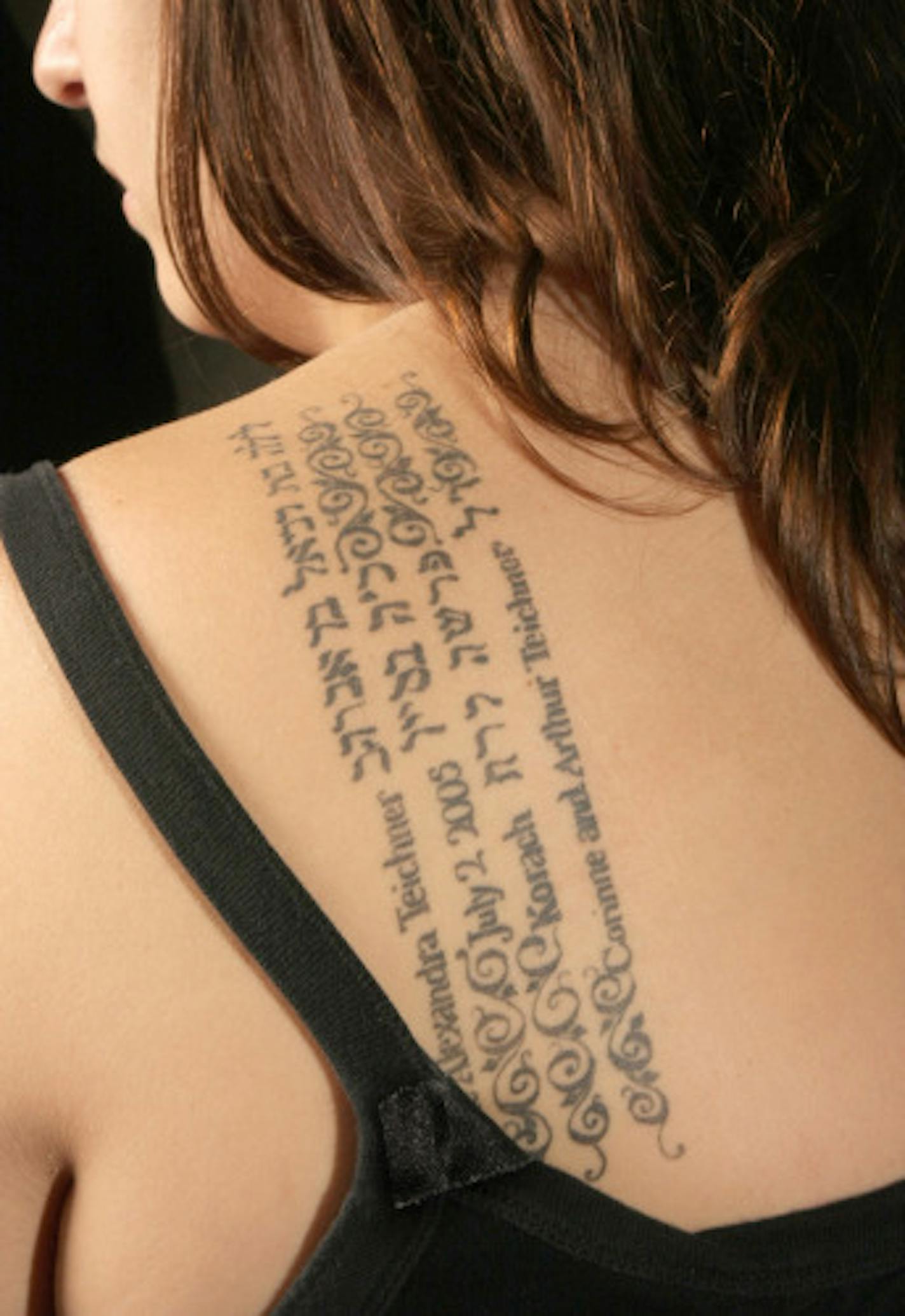 Melanie Teichner , close-up of the Hebrew tatoo on her back.shoulder , the lines are:, her name in Hebrew - Leila bat Daniel ben Avrum / date of her bat mitzvah, -Sivan 25 / weekly torah reading from her bat mitzvah - Korach / " In loving memory of Connie and Arthur Teichner", her grandparents.