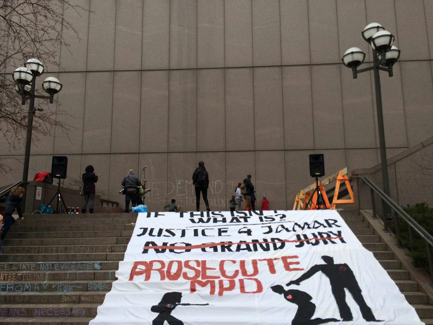 Children write "we demand justice" in chalk on the wall of the Hennepin County Government Center in front of a giant banner that reads "Prosecute MPD" before a rally Saturday in Minneapolis.