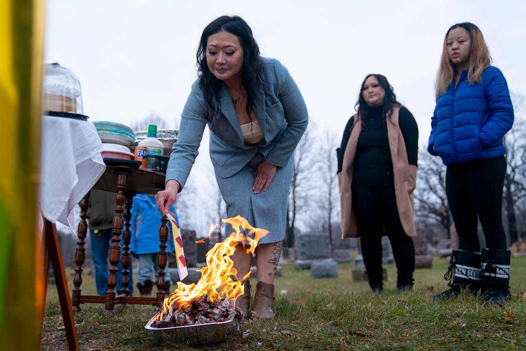 Baky Mikaele, with Jin’s family watching, burns 40 pieces of folded joss paper, or ghost money, at her son Jin Taylor’s grave at a primarily-Hmong cemetery in Chisago City on Dec. 16, 2023. In Hmong culture, the paper boats are meant to symbolize the boat floating away with the soul and are a form of currency in the spirit world.