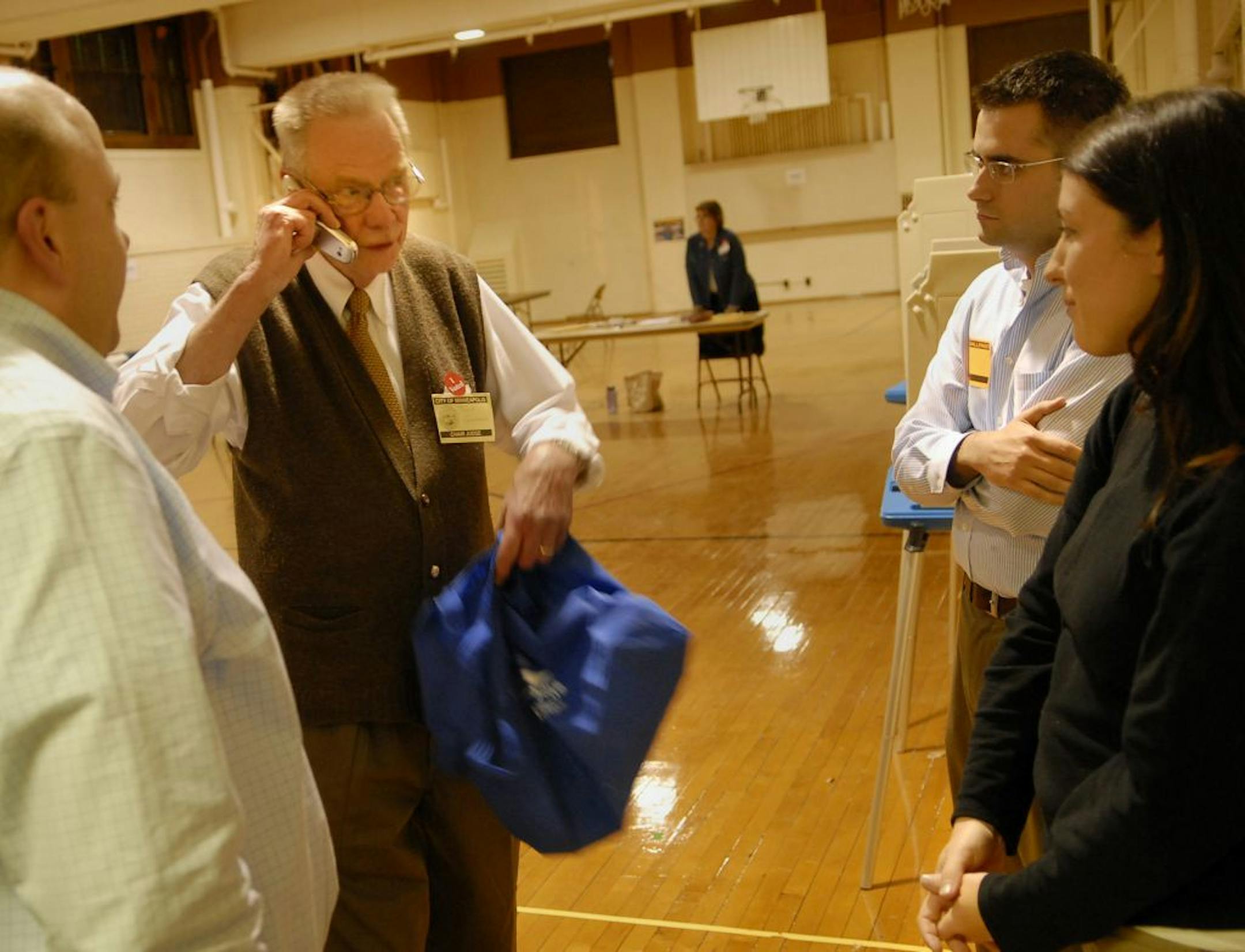 GLEN STUBBE � gstubbe@startribune.com Poll chair judge Tony Garners spoke to someone at state GOP headquarters on the cell phone of GOP poll watcher Leslie Wilcox, left. Standing next to her watching on the right is DFL poll watcher Chris Dolan. On the left is GOP poll watcher Jamie Wellik. Polls stayed open one hour late after a dispute over the utility bills used by U of M students to register to vote was resolved. NAMES TO COME