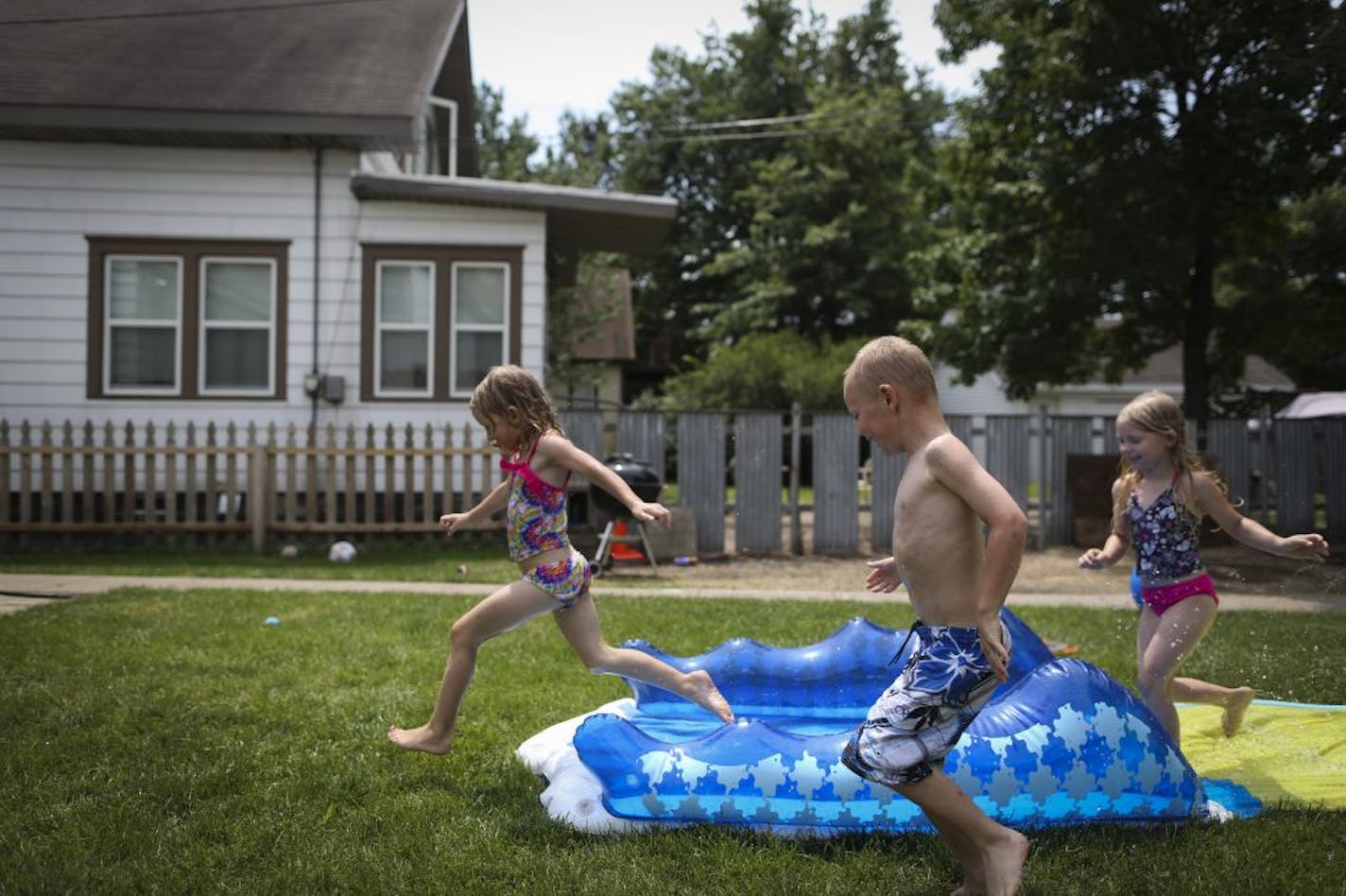 Karlee Mulligan, Brian Tiedens and Ava Mulligan played on a slip-n-slide in the backyard on Friday, June 29, 2012 in Minneapolis, Minn., a few blocks from where a 5-year-old boy was shot asleep on the couch in his house