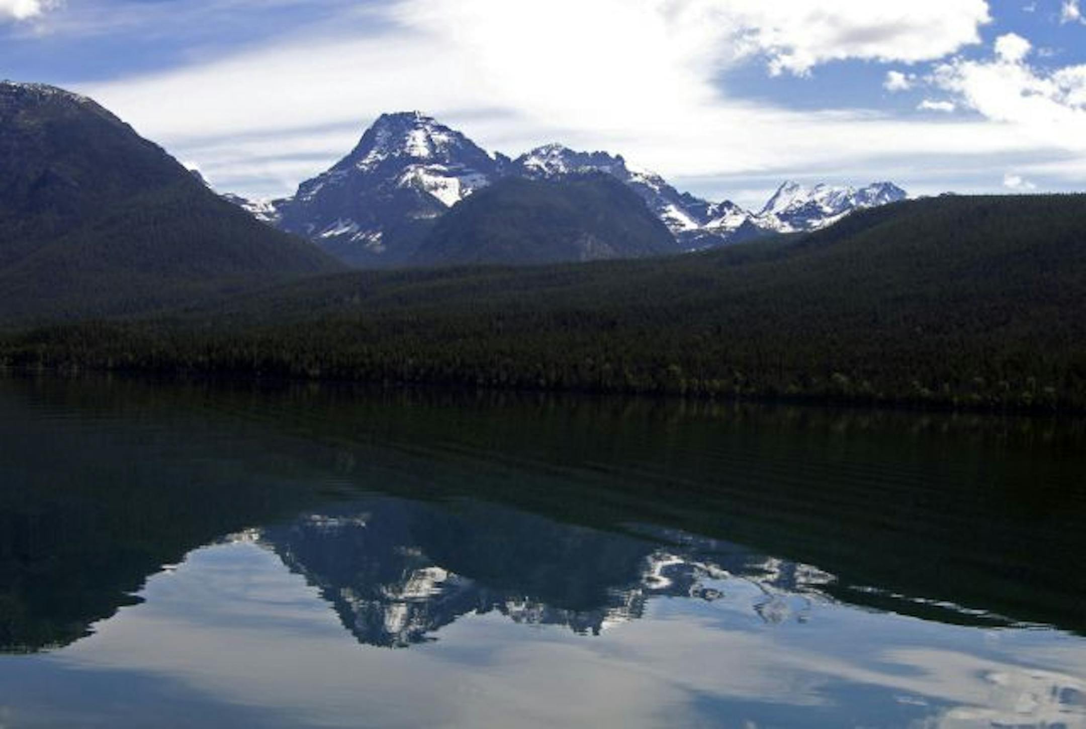 Rugged snow-capped mountains reflect off a pristine lake in Glacier National Park.