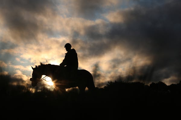 Exercise riders make their way to the track for a morning ride as the sun's first rays of the day light up the cloud filled sky at Canterbury Park. Im