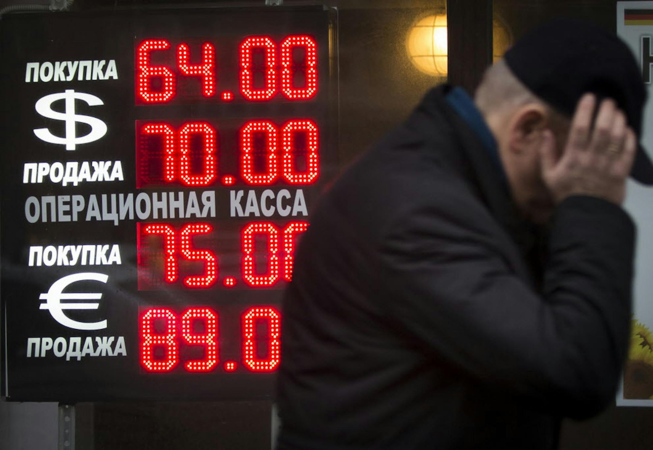 FILE - In this Tuesday, Dec. 16, 2014, file photo, a man walks by a sign advertising currencies of an exchange office in Moscow. Russia has been badly affected by the slide in oil prices in 2014, and the ruble has plunged despite big increases in interest rates as much of Russia's economy is based on energy. (AP Photo/Alexander Zemlianichenko, File )